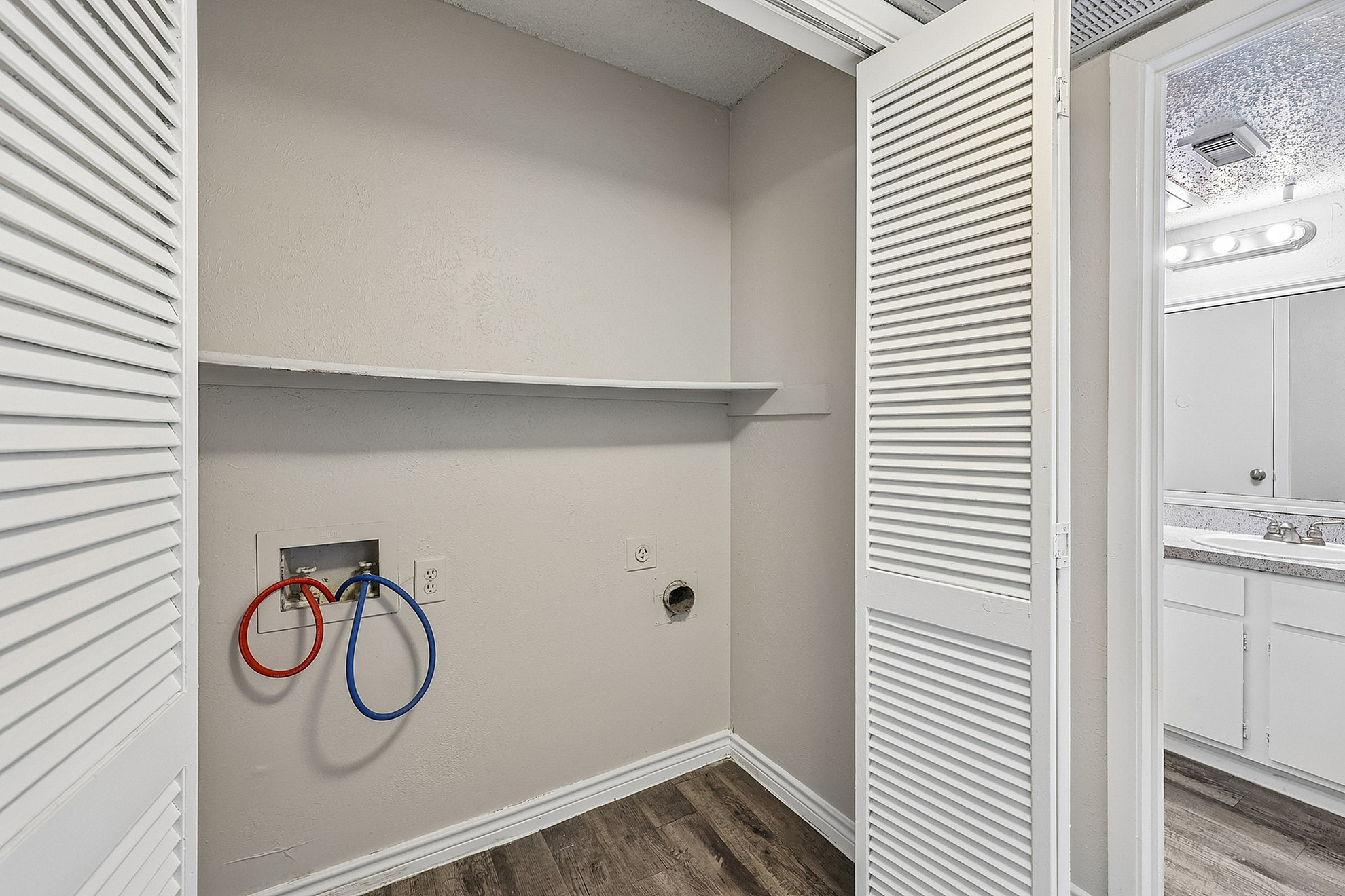 Inviting laundry nook with bi-fold doors and ample shelving, adjacent to a bright bathroom with modern fixtures.
