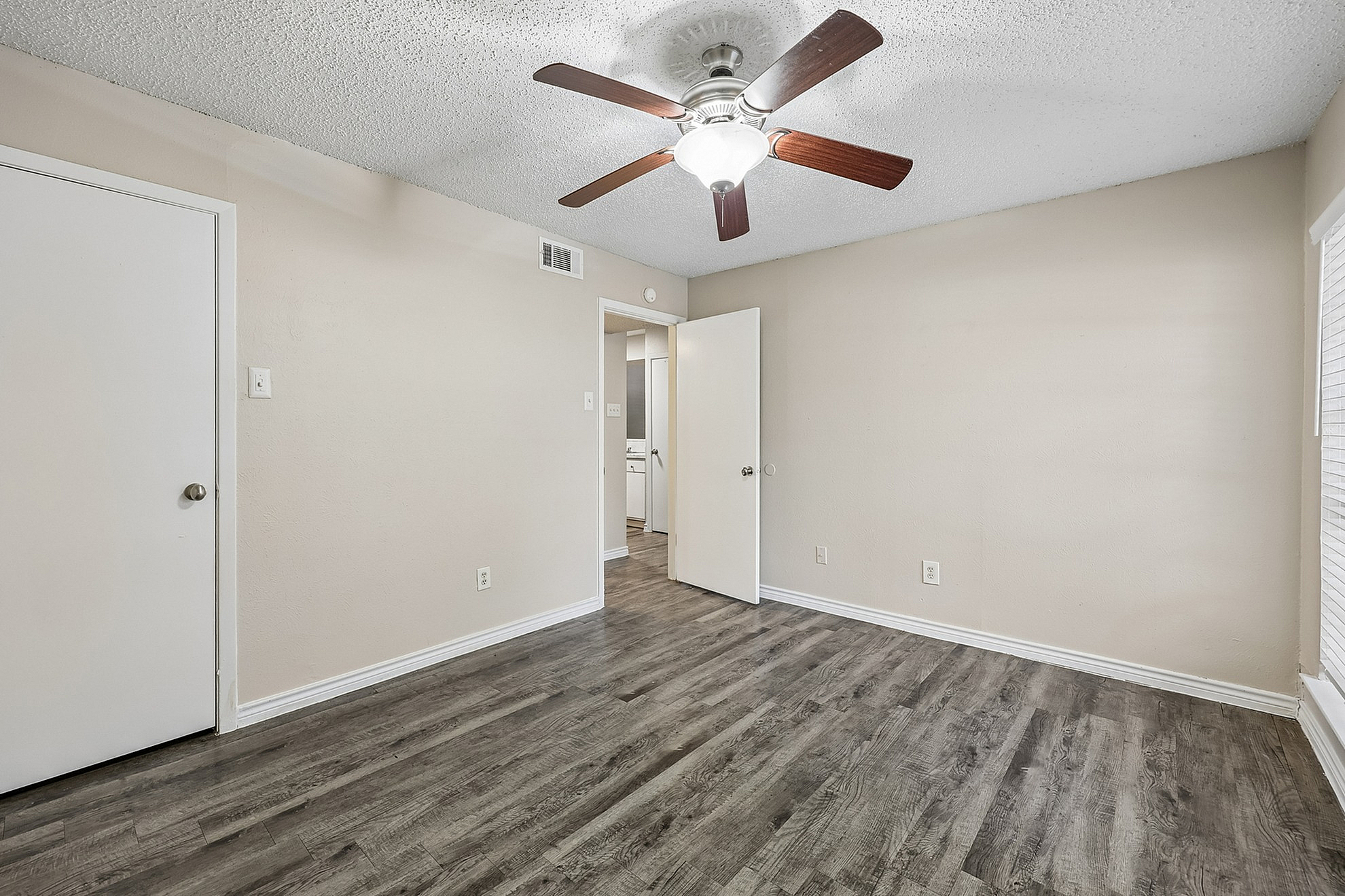 Inviting bedroom with stylish wood flooring, neutral walls, and a ceiling fan, offering a cozy ambiance.