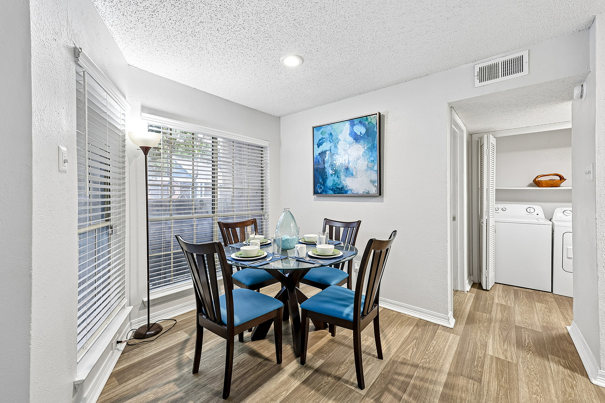 Charming dining nook with a modern round table, blue cushioned chairs, and contemporary art, adjacent to a convenient laundry area with washer and dryer.