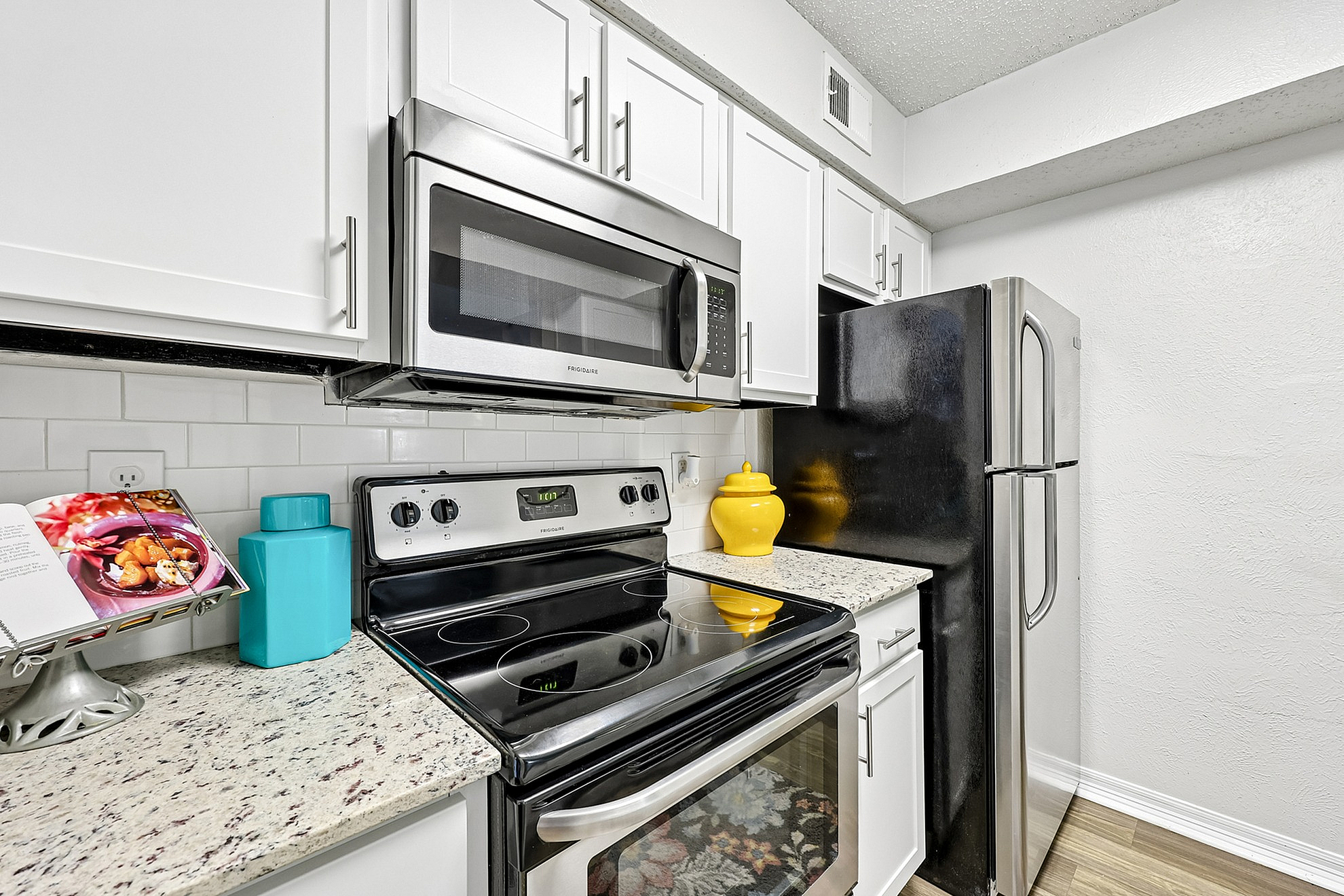 Modern kitchen with stainless steel appliances, chic white cabinets, and granite countertops, enhanced by colorful decor accents.