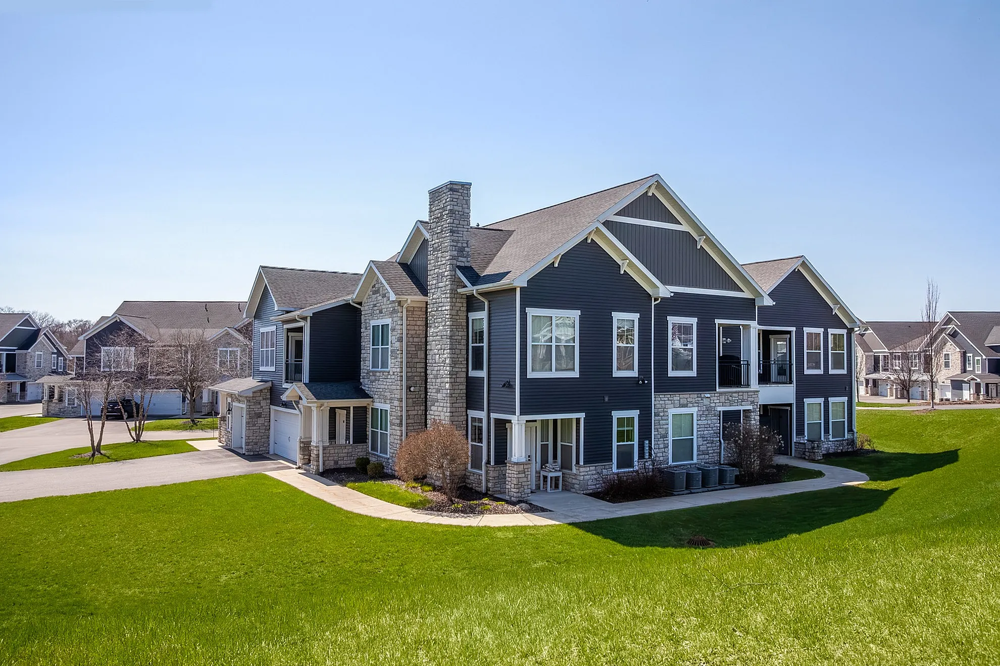 Elegant modern apartment complex with stone accents and lush green surroundings, featuring spacious balconies and large windows.