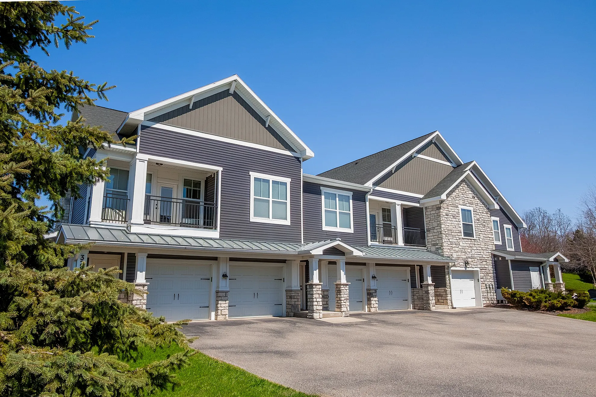 Charming modern townhouse with stone accents, featuring spacious balconies and a neatly maintained driveway under a clear blue sky.