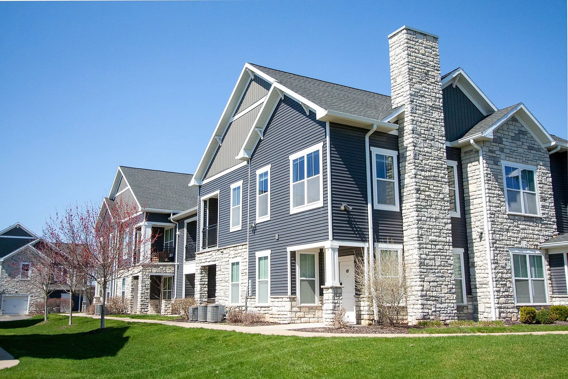 Charming modern apartments with elegant stone and siding facade, nestled in a beautifully landscaped neighborhood.