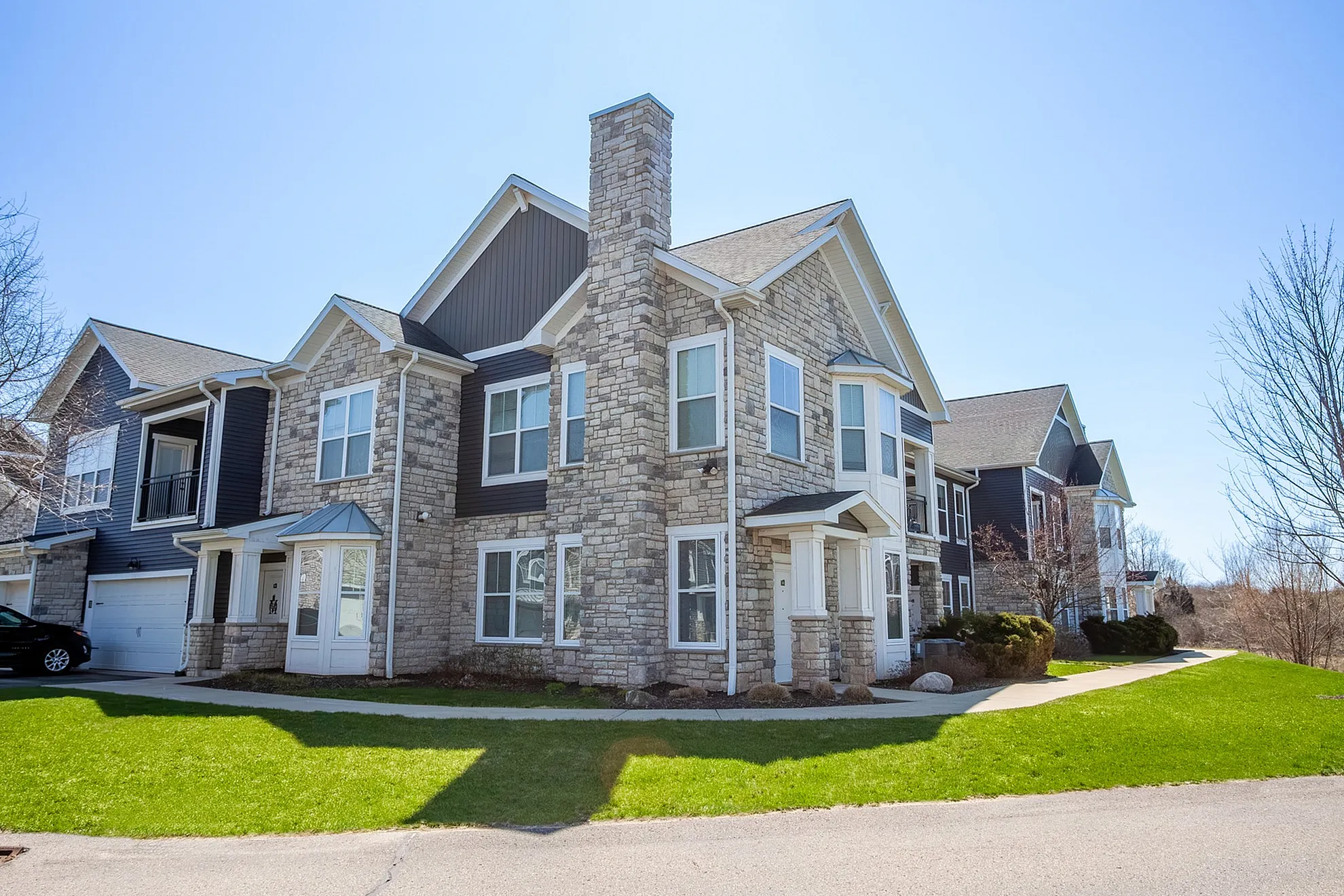 Charming stone-facade apartment complex with large windows and lush green surroundings, showcasing modern architectural design.