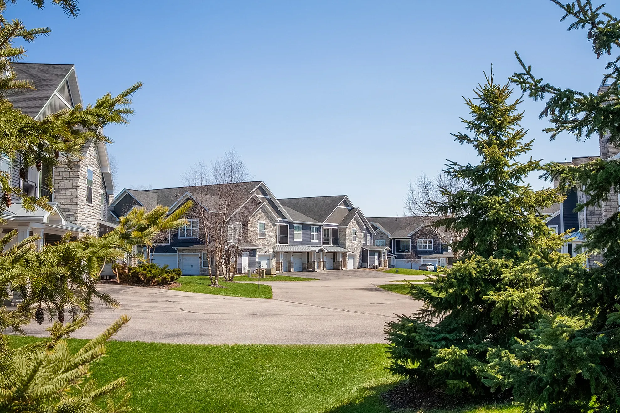 Charming suburban neighborhood with modern townhouses, surrounded by lush greenery and a clear blue sky.