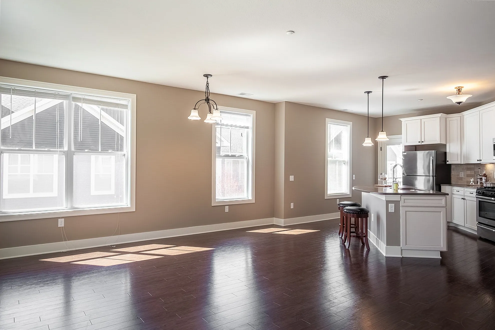 Bright, modern open-plan living area with sleek hardwood floors, expansive windows, and a stylish kitchen island with bar stools.