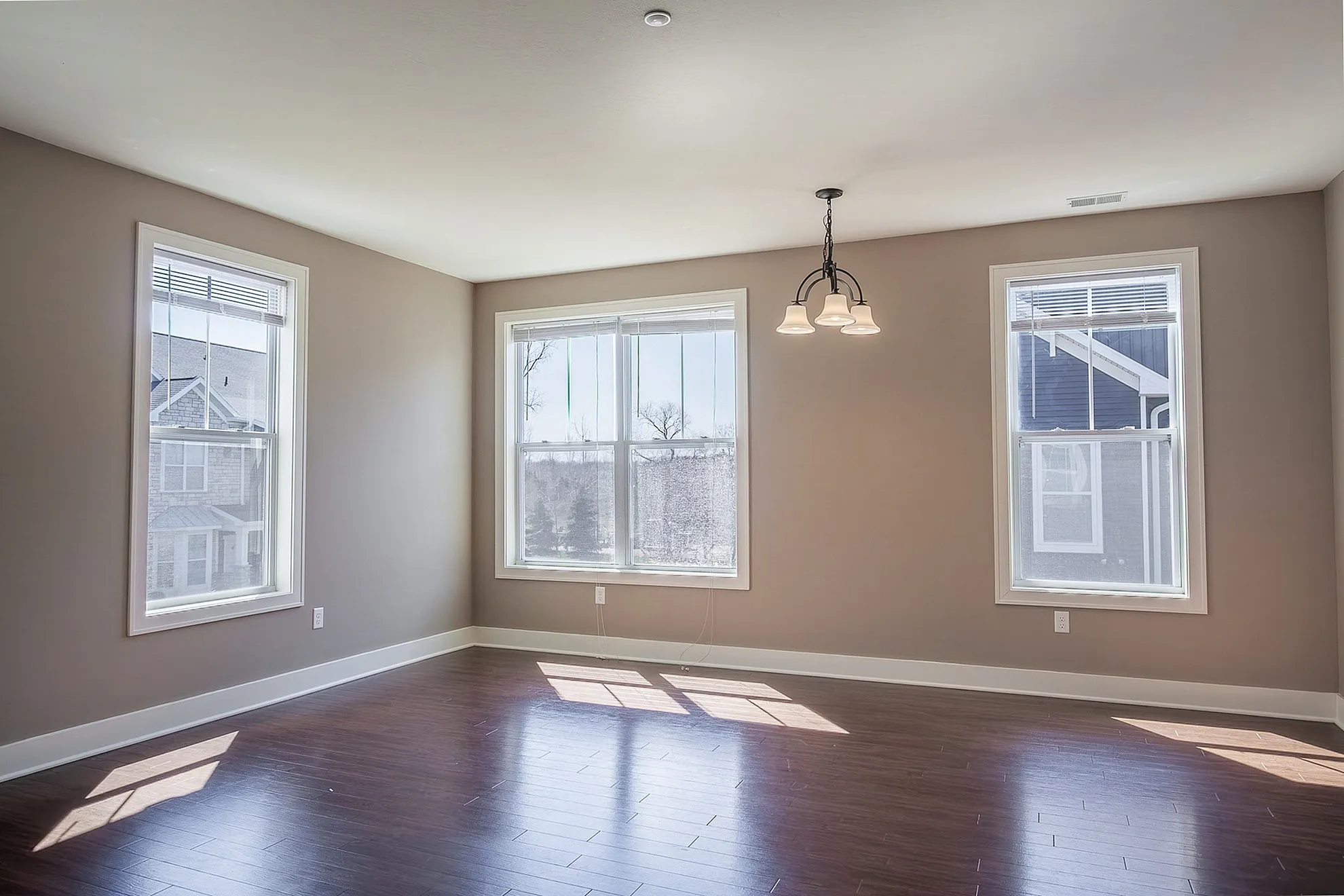 Bright and airy empty room with elegant hardwood flooring and large windows, perfect for a cozy living area.