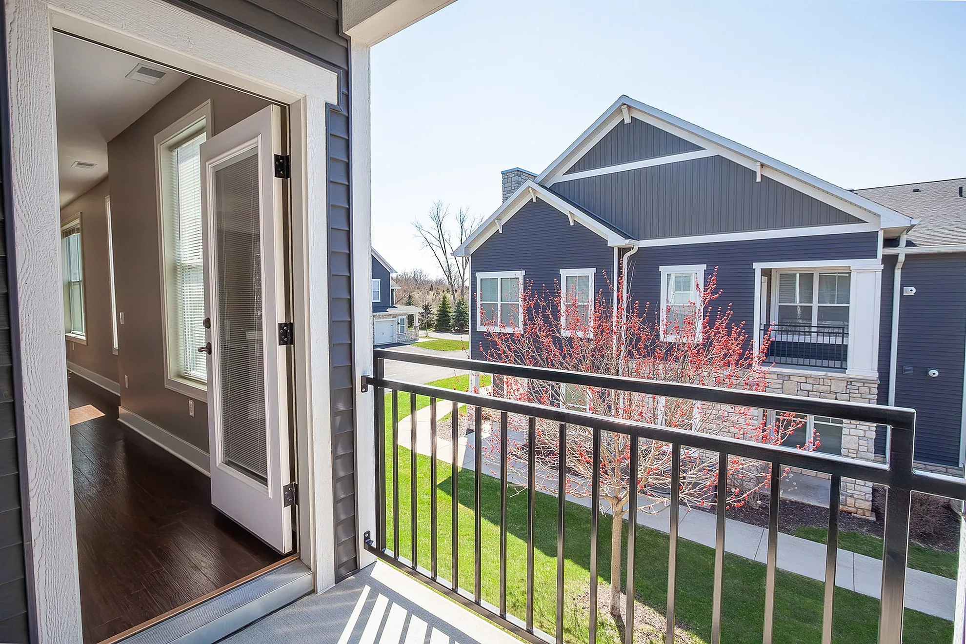 Bright second-floor view from a modern apartment balcony overlooking landscaped greenery and elegant architecture.