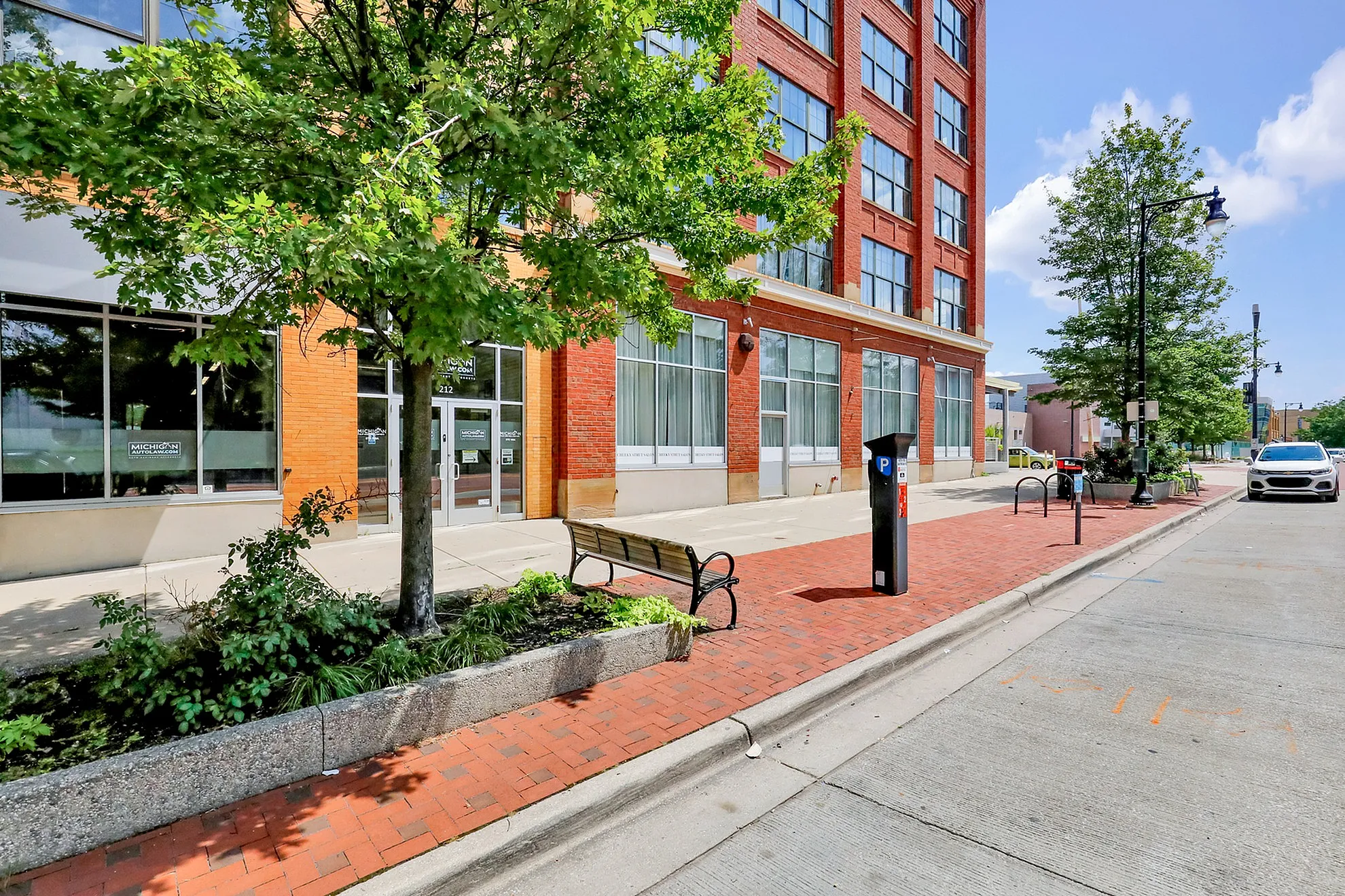 Charming urban building with red brick facade, large windows, and a tree-lined sidewalk, perfect for a vibrant city lifestyle.