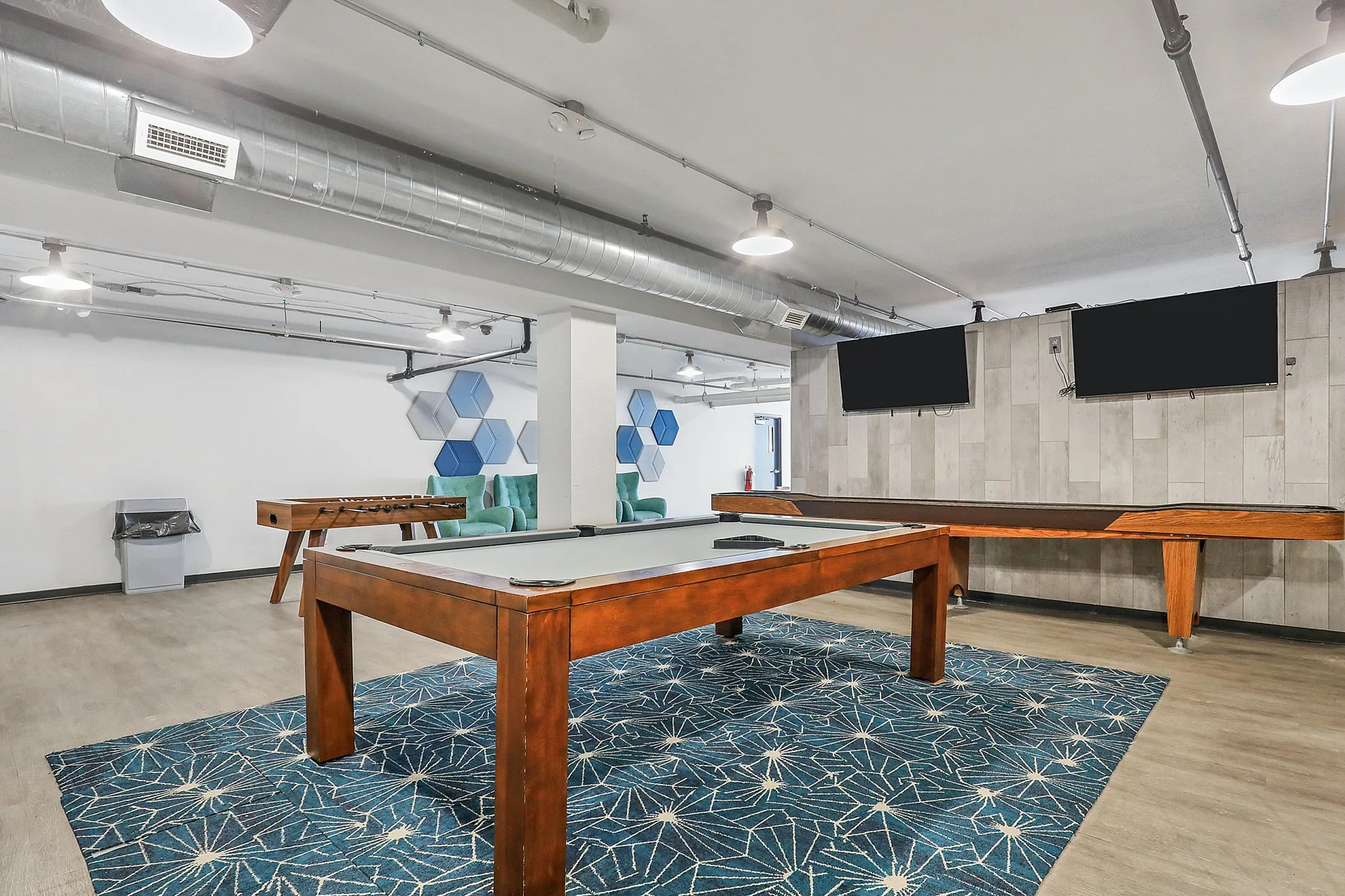 Modern recreational room featuring sleek billiards and foosball tables, vibrant wall art, and flat-screen TVs for a fun and stylish entertainment experience.