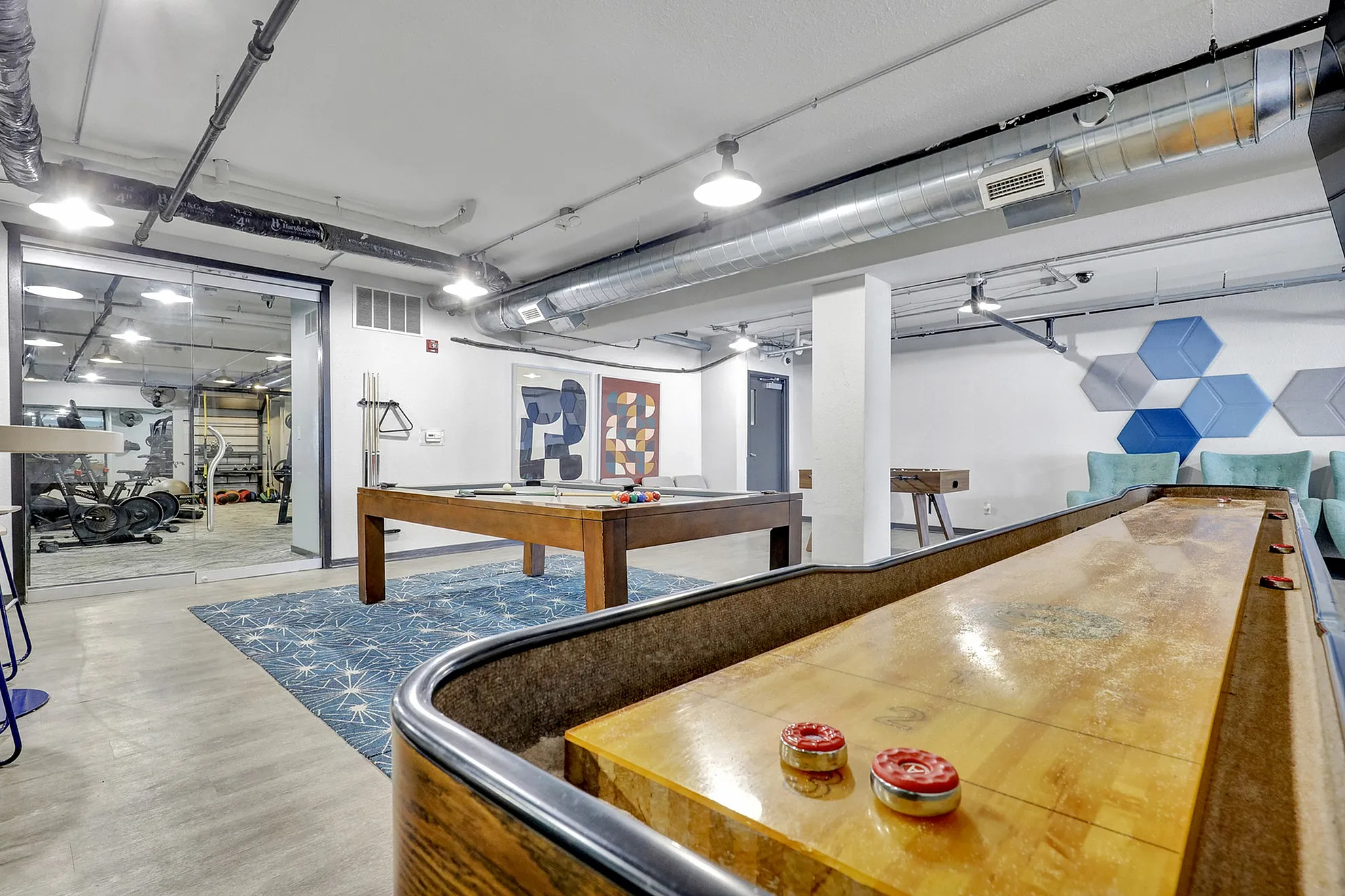 Modern recreational room featuring a shuffleboard table, pool table, and gym access, perfect for leisure and fitness.