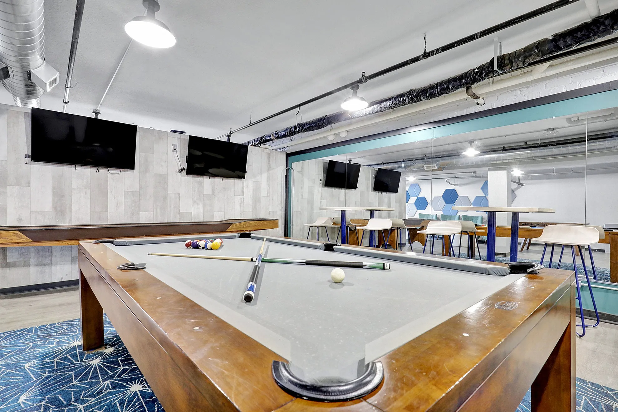 Modern game room with a sleek pool table, multiple TVs, and stylish seating area, perfect for entertainment and relaxation.