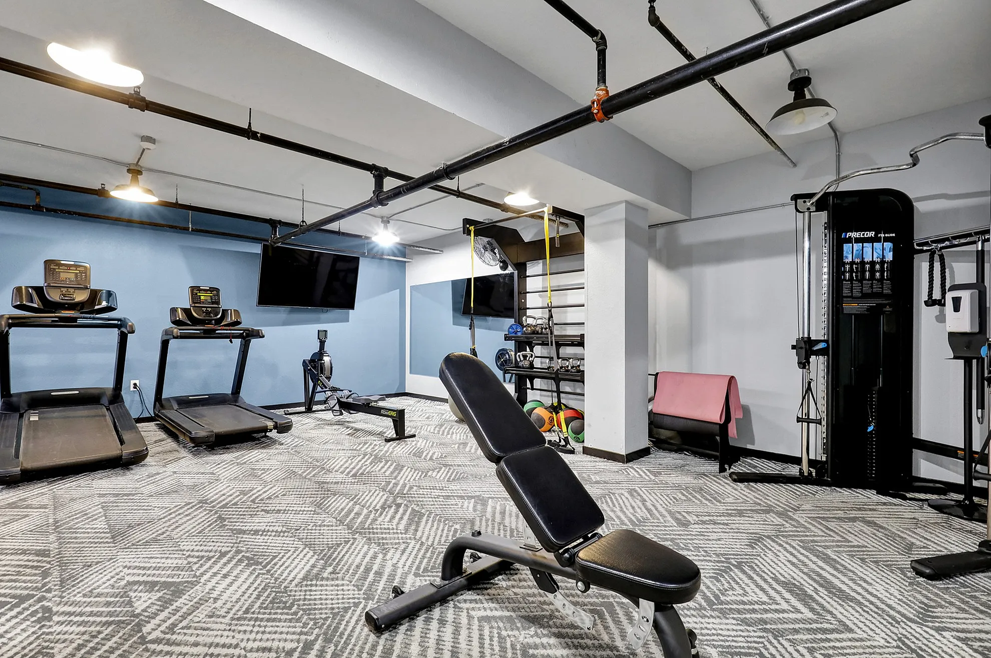 Modern fitness room featuring treadmills, exercise bench, rowing machine, and a variety of workout equipment on stylish patterned flooring.