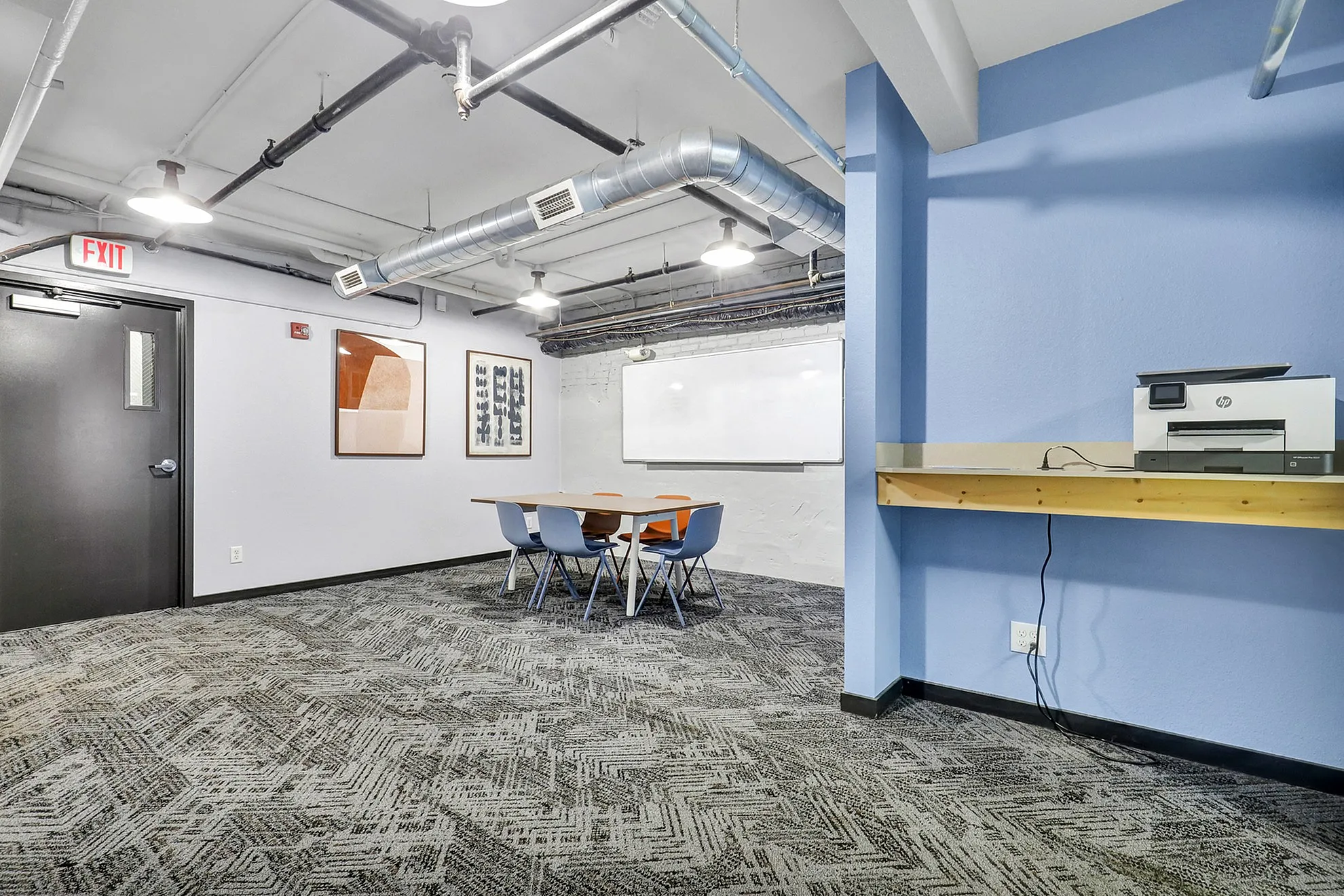Modern office space featuring a stylish table, vibrant artwork, whiteboard, and convenient printer station. Ideal for creative meetings and productive work.