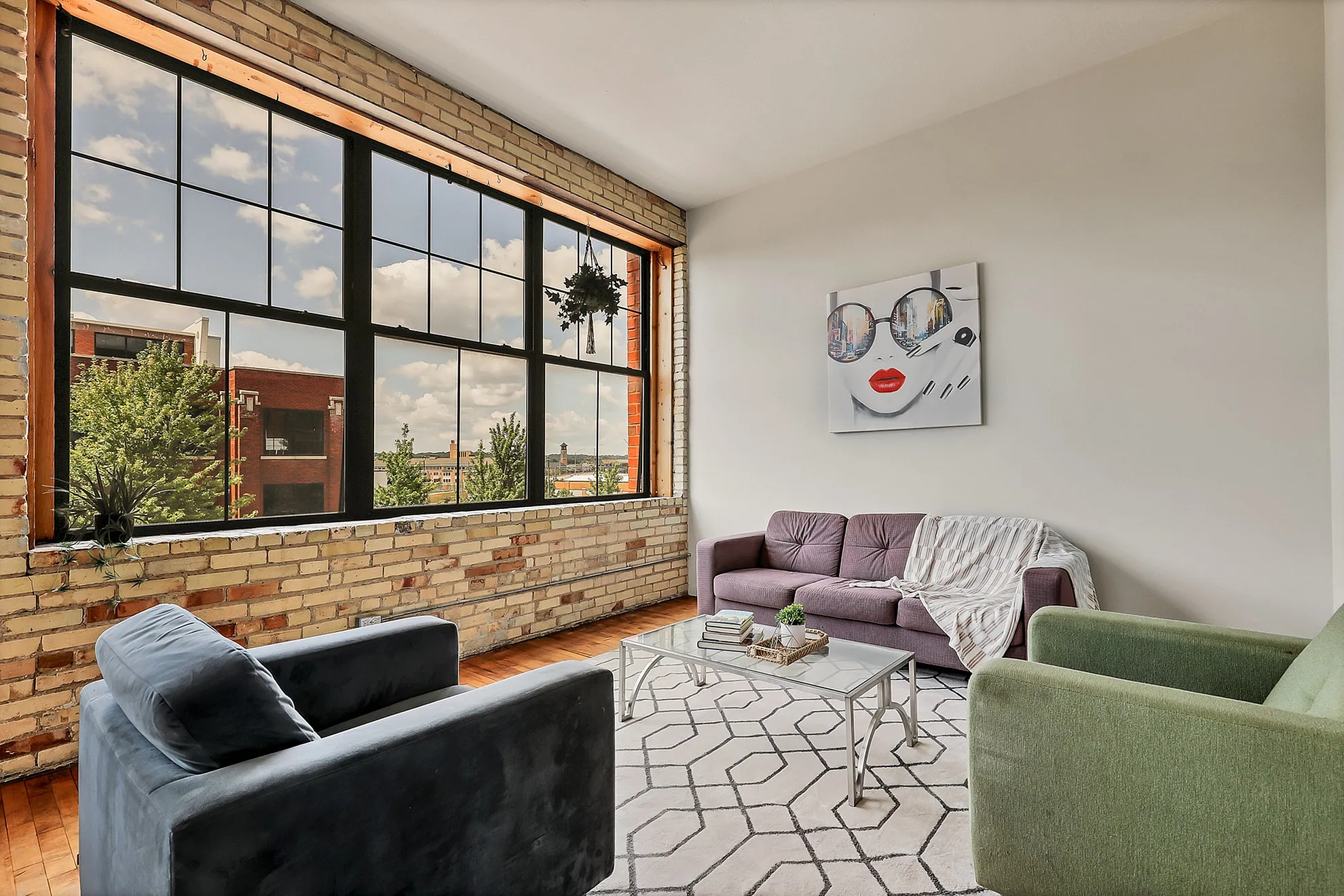 Chic urban living room with exposed brick walls, large industrial-style windows, and stylish modern furniture offering a cozy ambiance and vibrant city views.