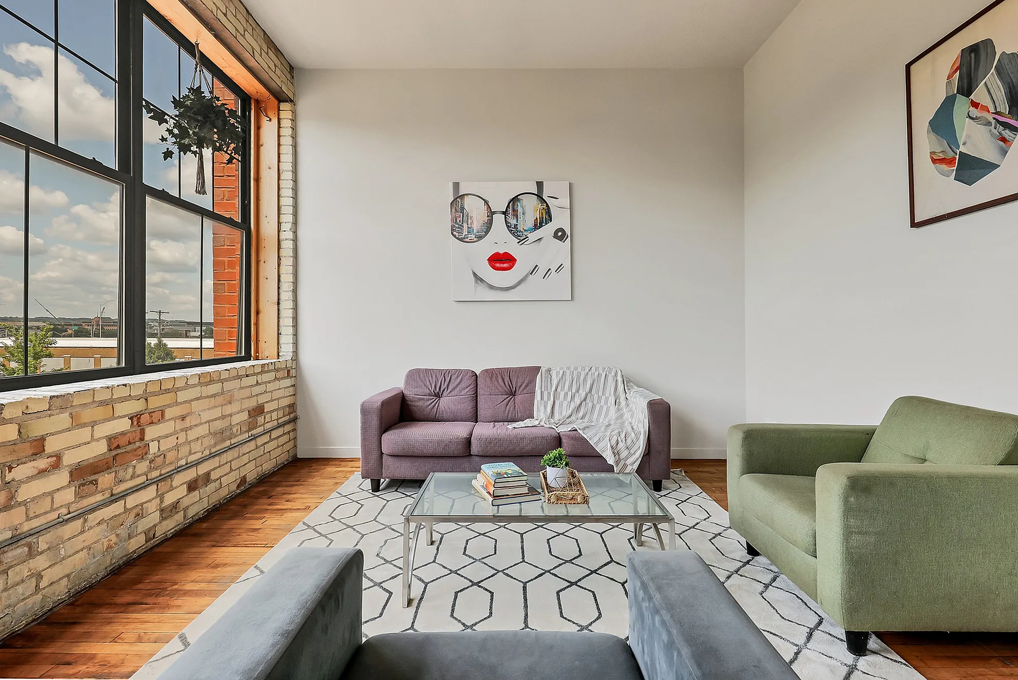 Chic urban living room with large windows, vibrant artwork, and modern furniture, bathed in natural light.