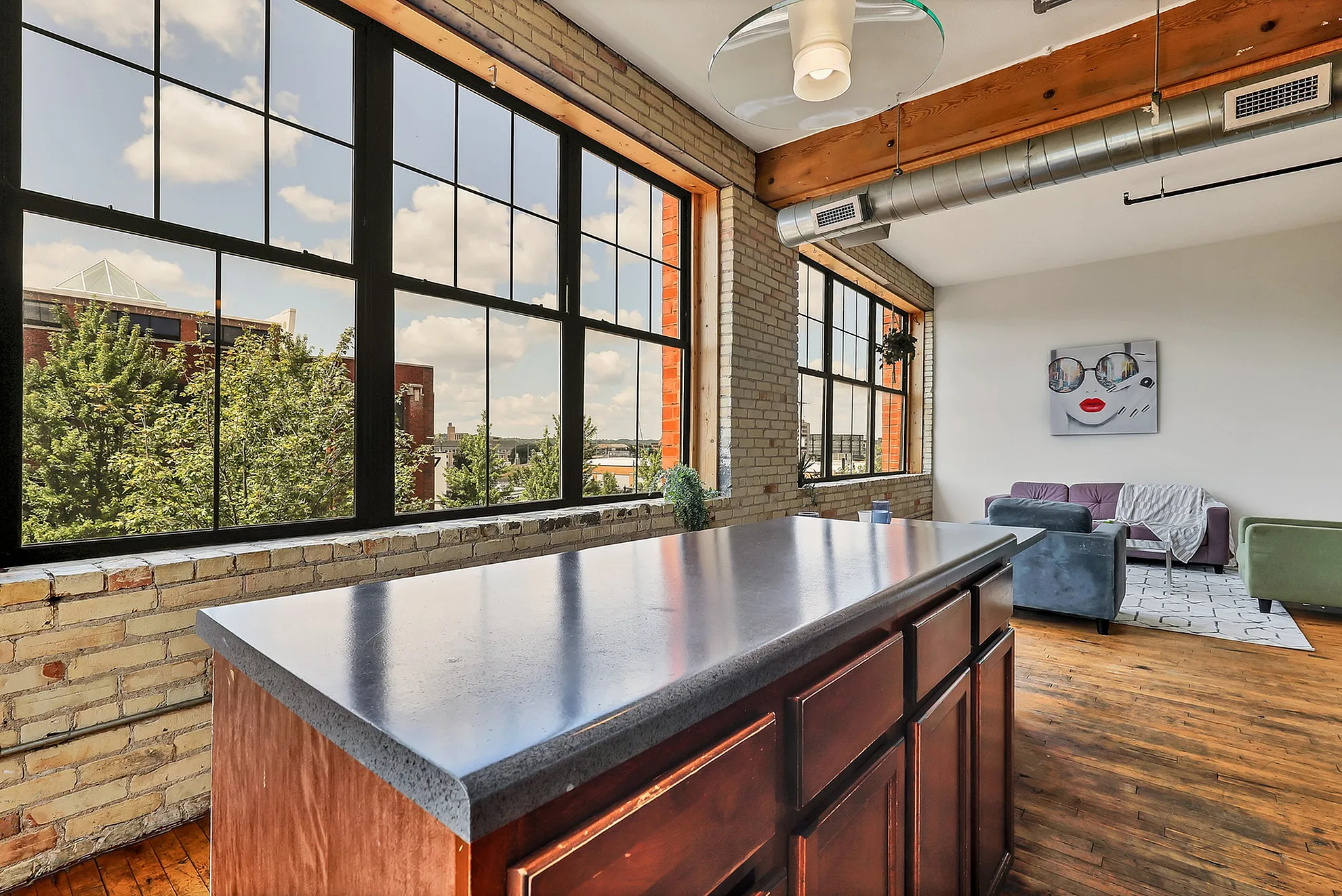 Chic urban loft with expansive windows, modern kitchen island, and vibrant living area, offering cityscape views.