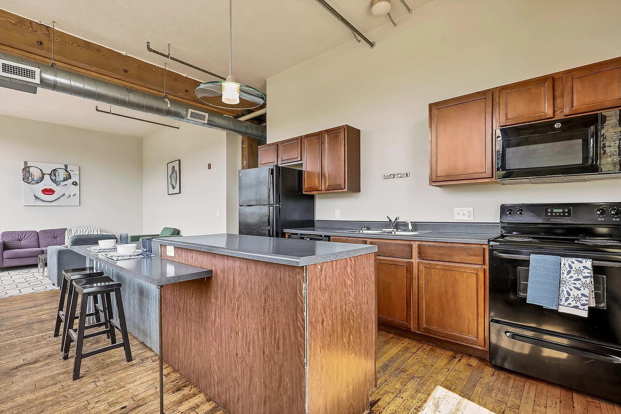 Modern open-concept kitchen and living area with sleek wood cabinets, rustic wood flooring, and chic industrial accents.