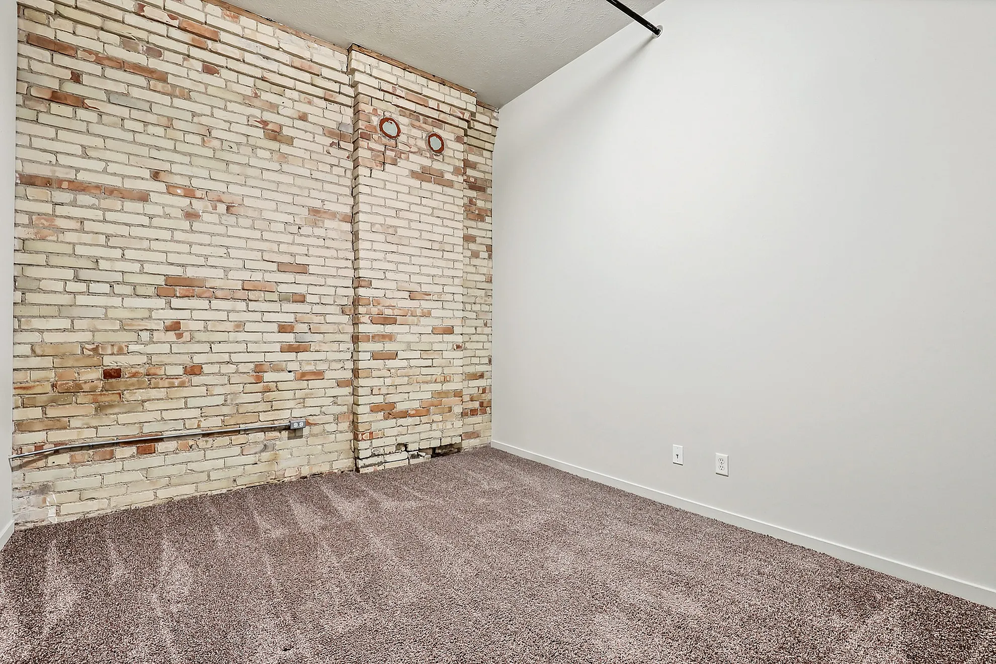 Charming apartment space featuring a rustic exposed brick wall and plush carpeting, perfect for cozy urban living.