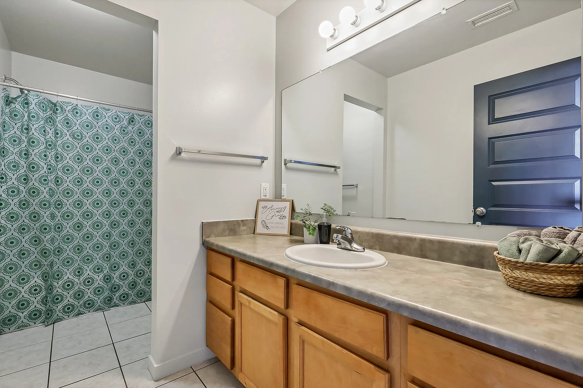 Bright and modern bathroom featuring sleek light fixtures, a spacious mirror, and stylish green shower curtain.