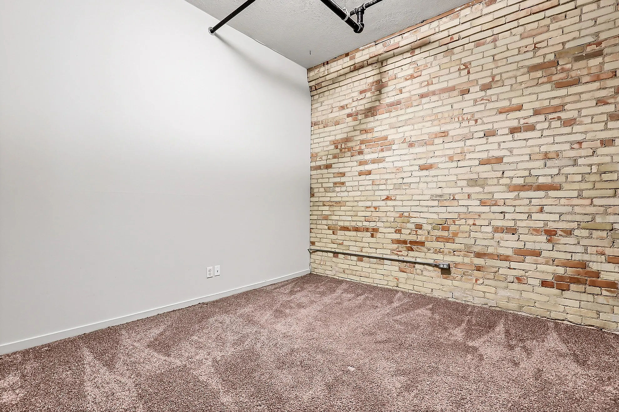 Charming room featuring an exposed brick wall and plush carpet, perfect for a cozy and stylish living space.