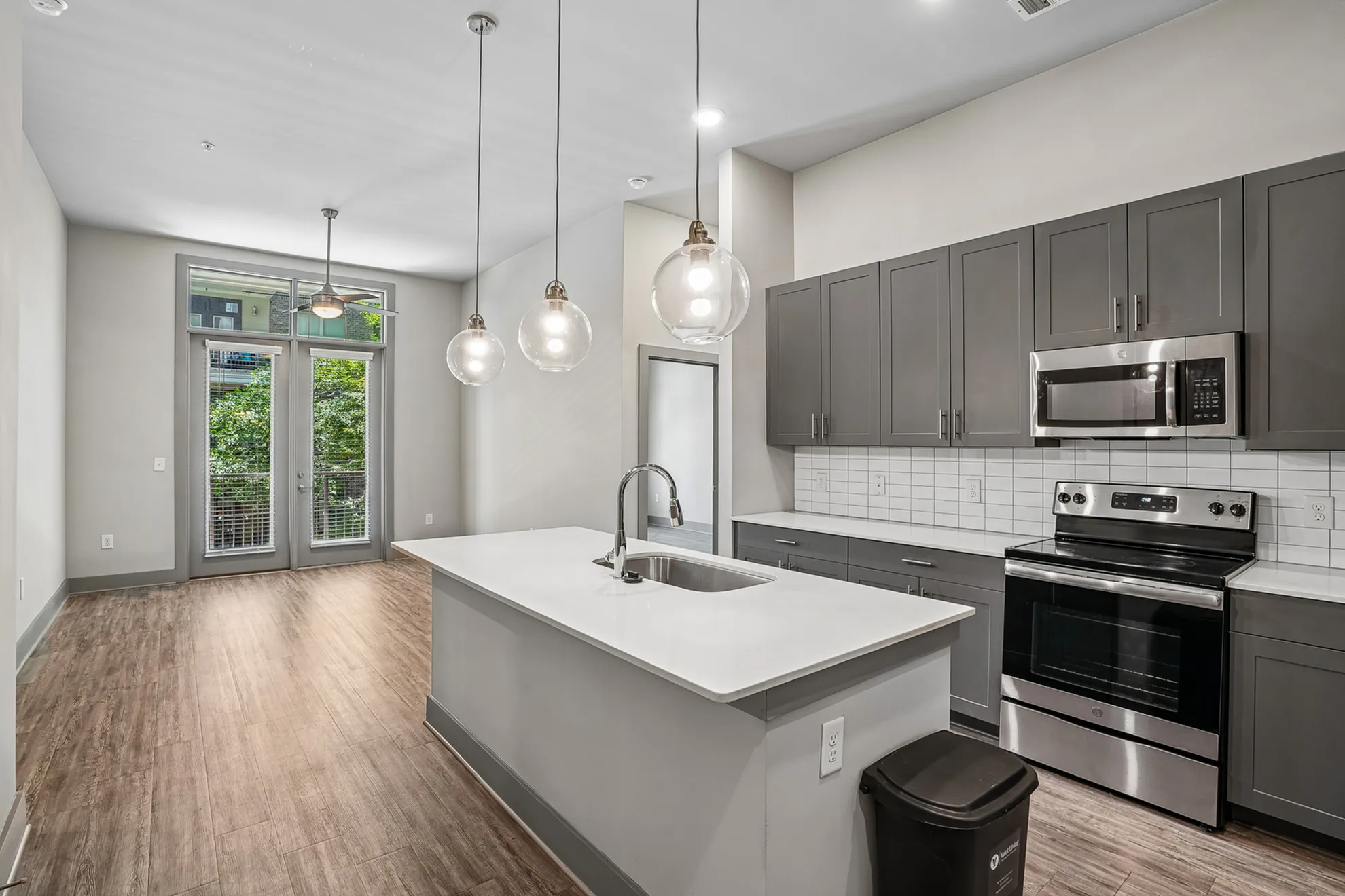 Modern kitchen featuring sleek countertops, stylish pendant lighting, and stainless steel appliances with patio access.