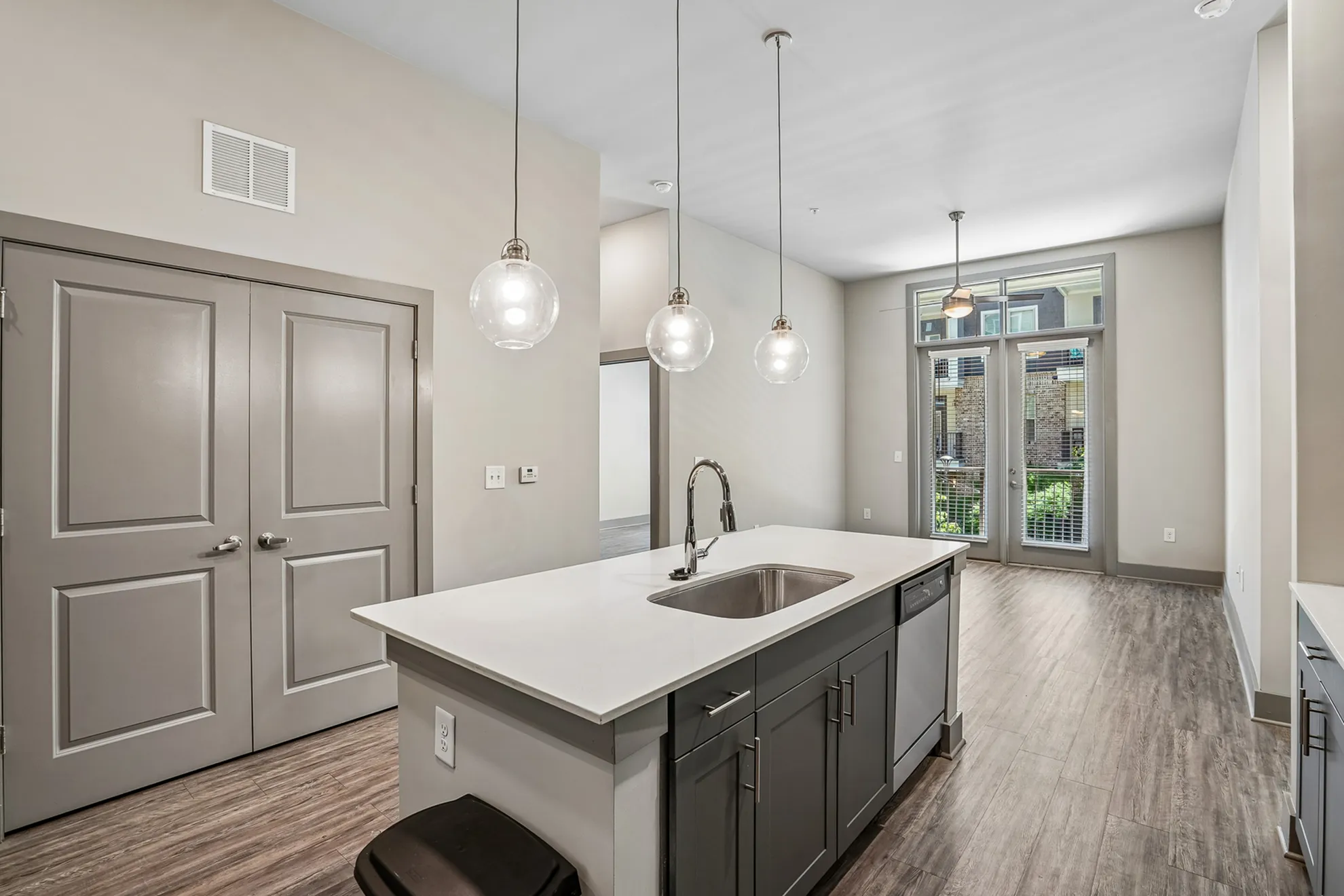 Modern kitchen space with sleek countertops, pendant lighting, and ample natural light from large glass doors.