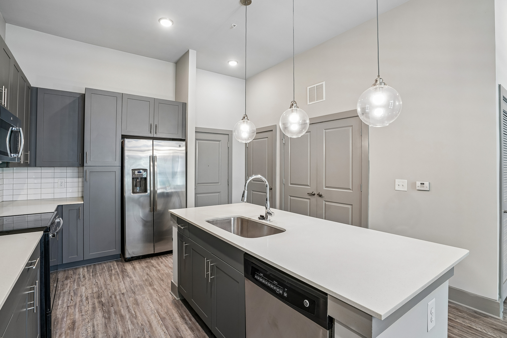 Modern kitchen with sleek gray cabinets, stainless steel appliances, and elegant pendant lighting over a spacious island.