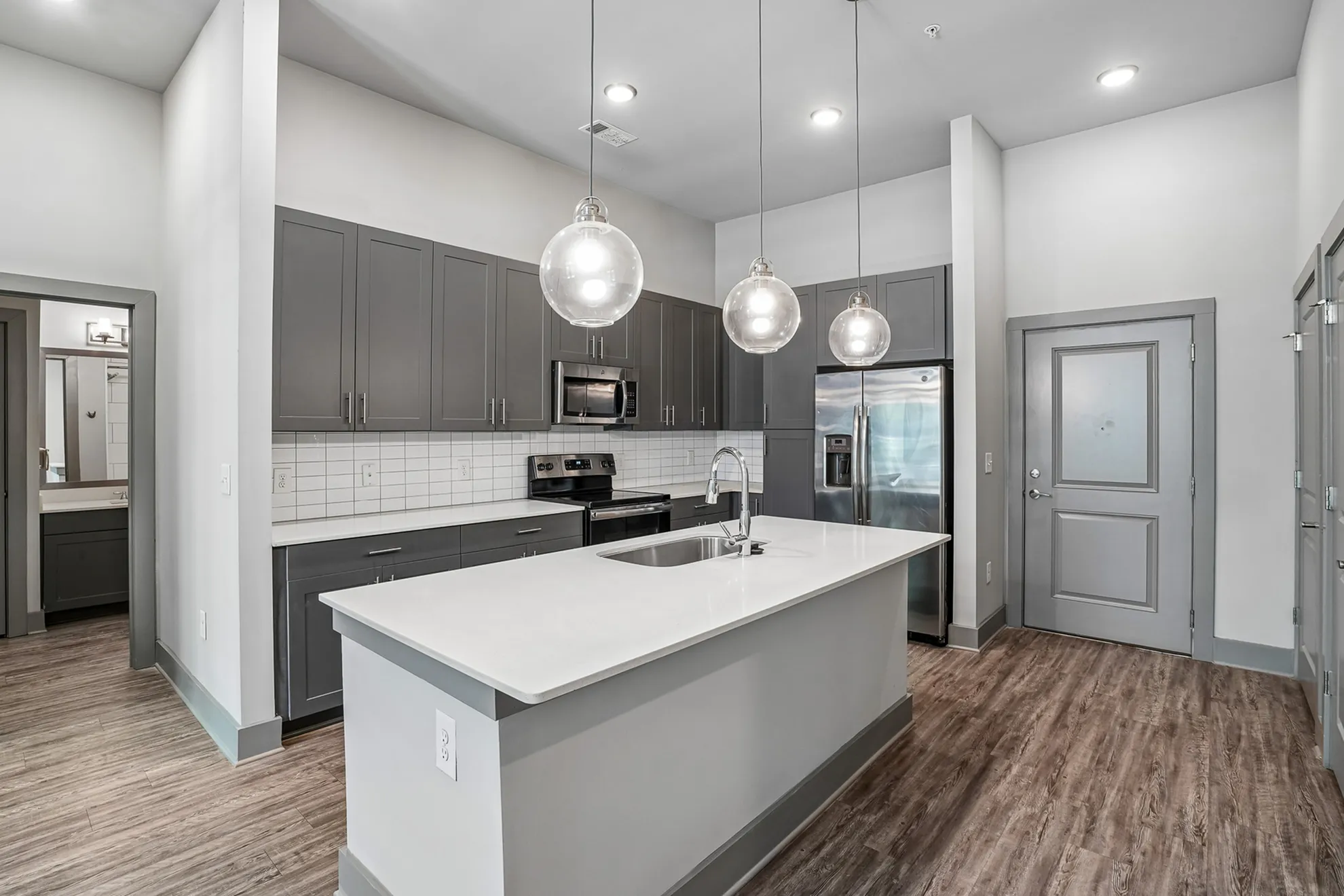 Modern kitchen with sleek gray cabinetry, stainless steel appliances, and elegant pendant lighting over a spacious white island.