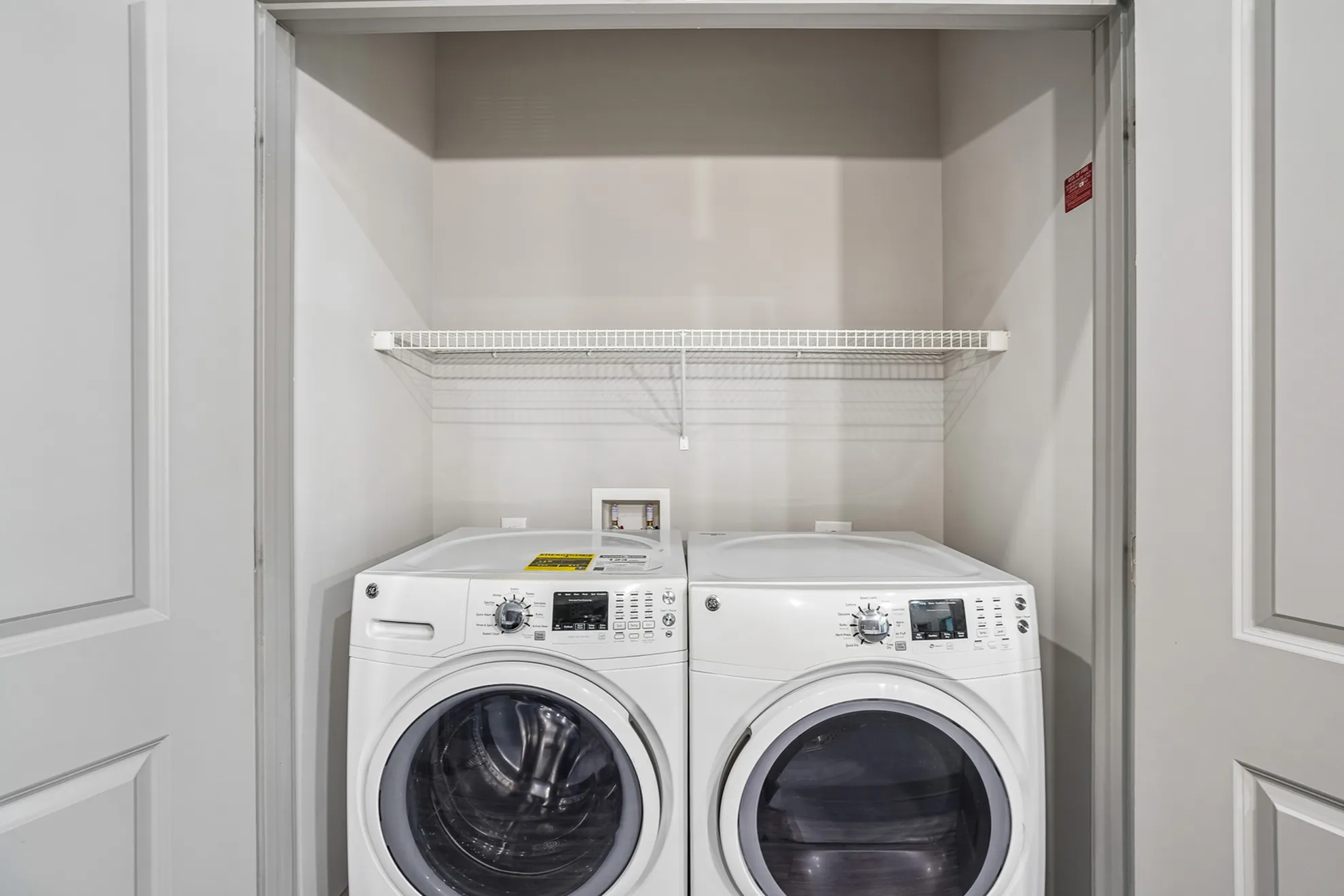 Modern apartment laundry closet featuring a sleek front-loading washer and dryer set with convenient overhead shelving.