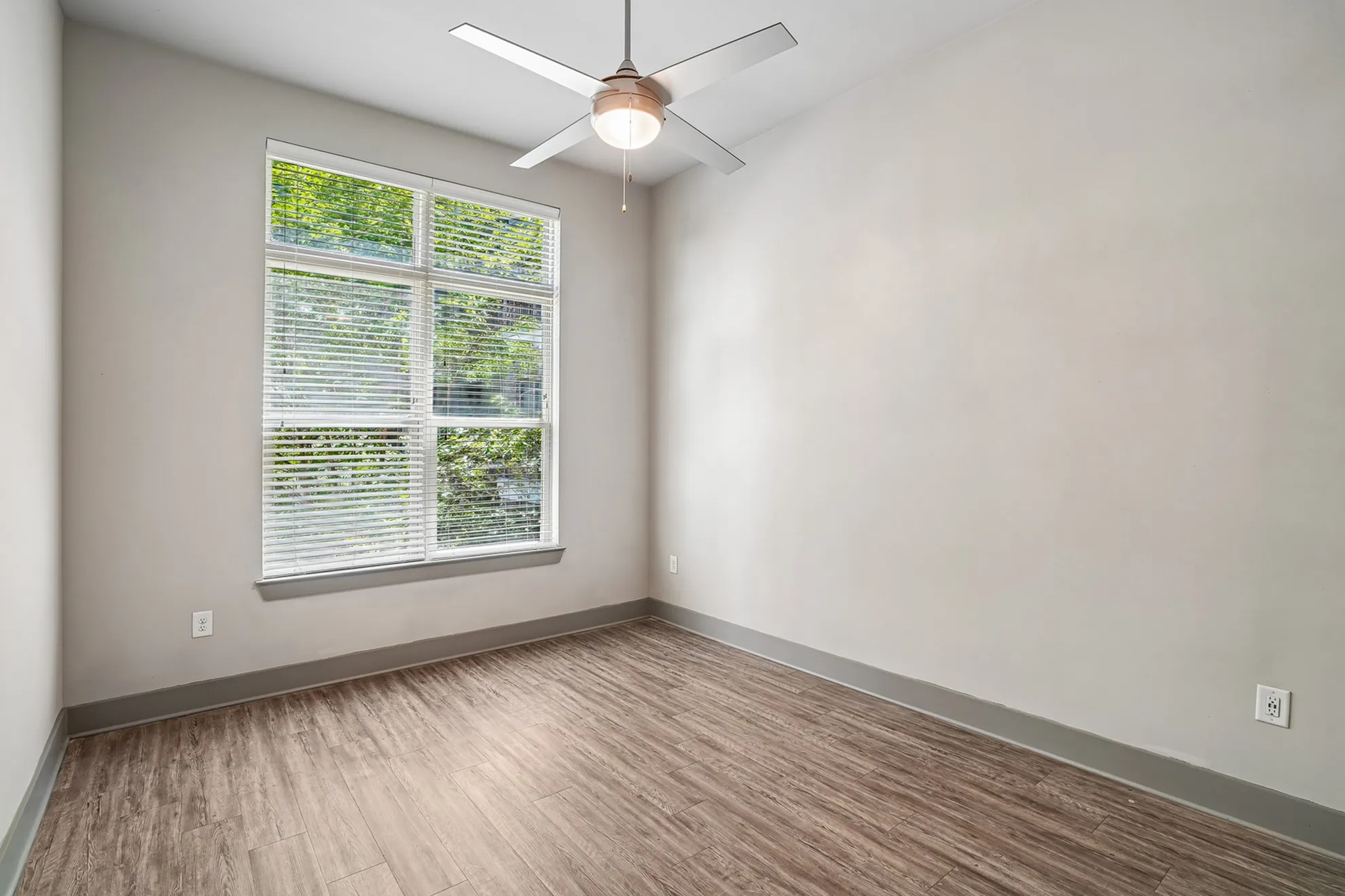 Bright room featuring hardwood floors, a large window with lush outdoor views, and a modern ceiling fan.