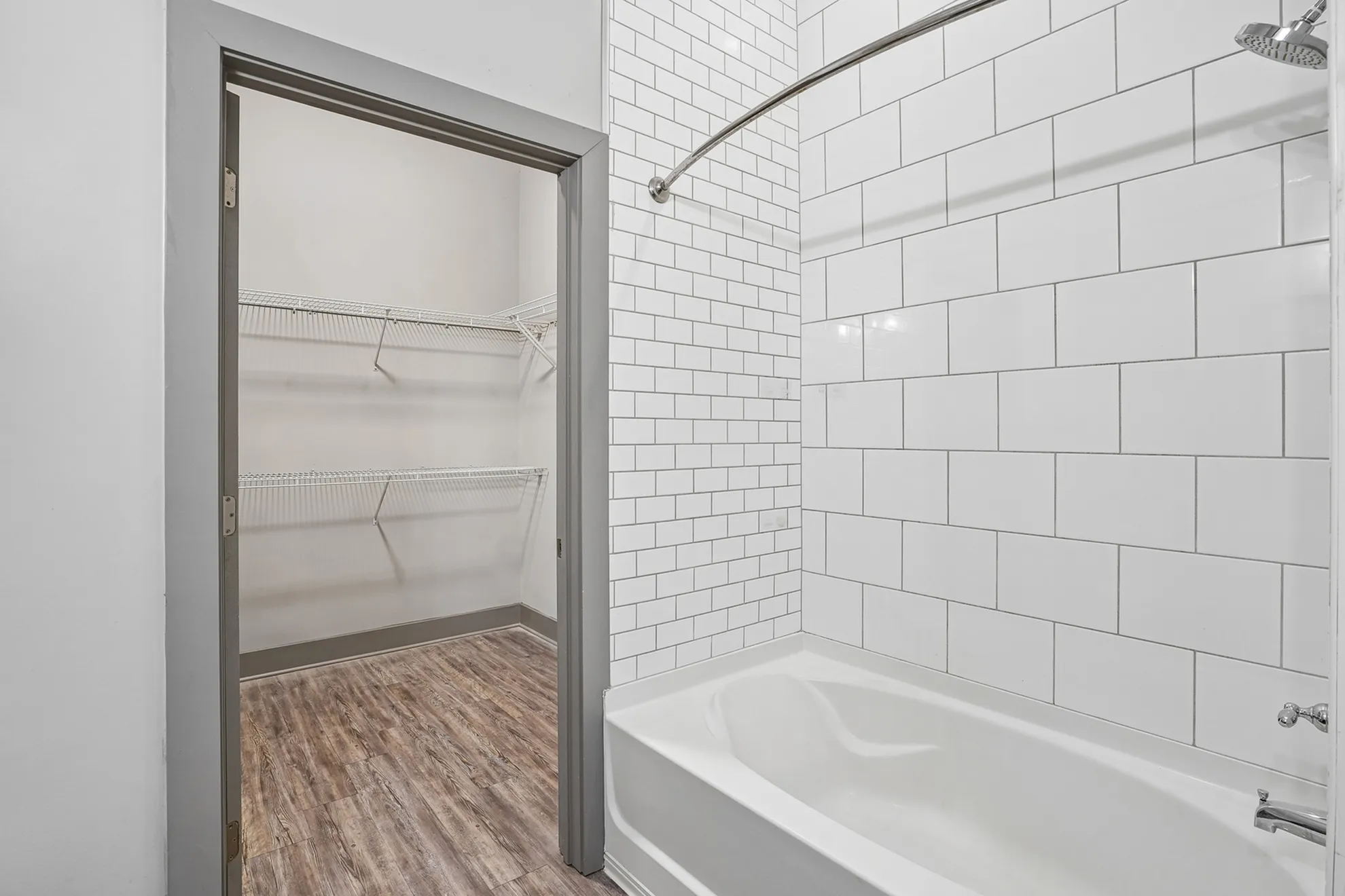 Modern bathroom featuring elegant white subway tile design, a luxurious bathtub, and spacious walk-in closet with wooden flooring.