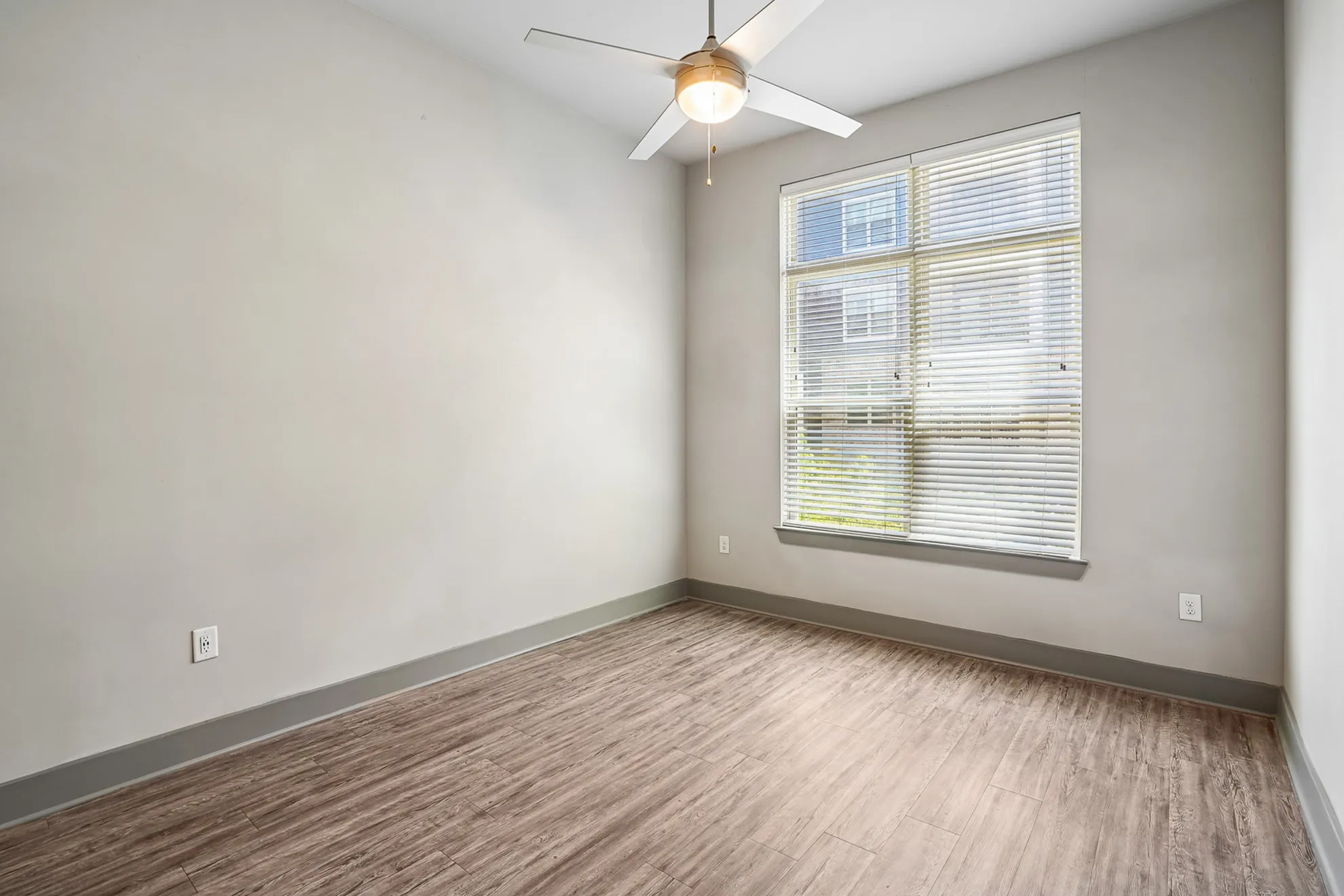 Bright, spacious room with modern wooden flooring and a large window featuring adjustable blinds, ideal for natural light.