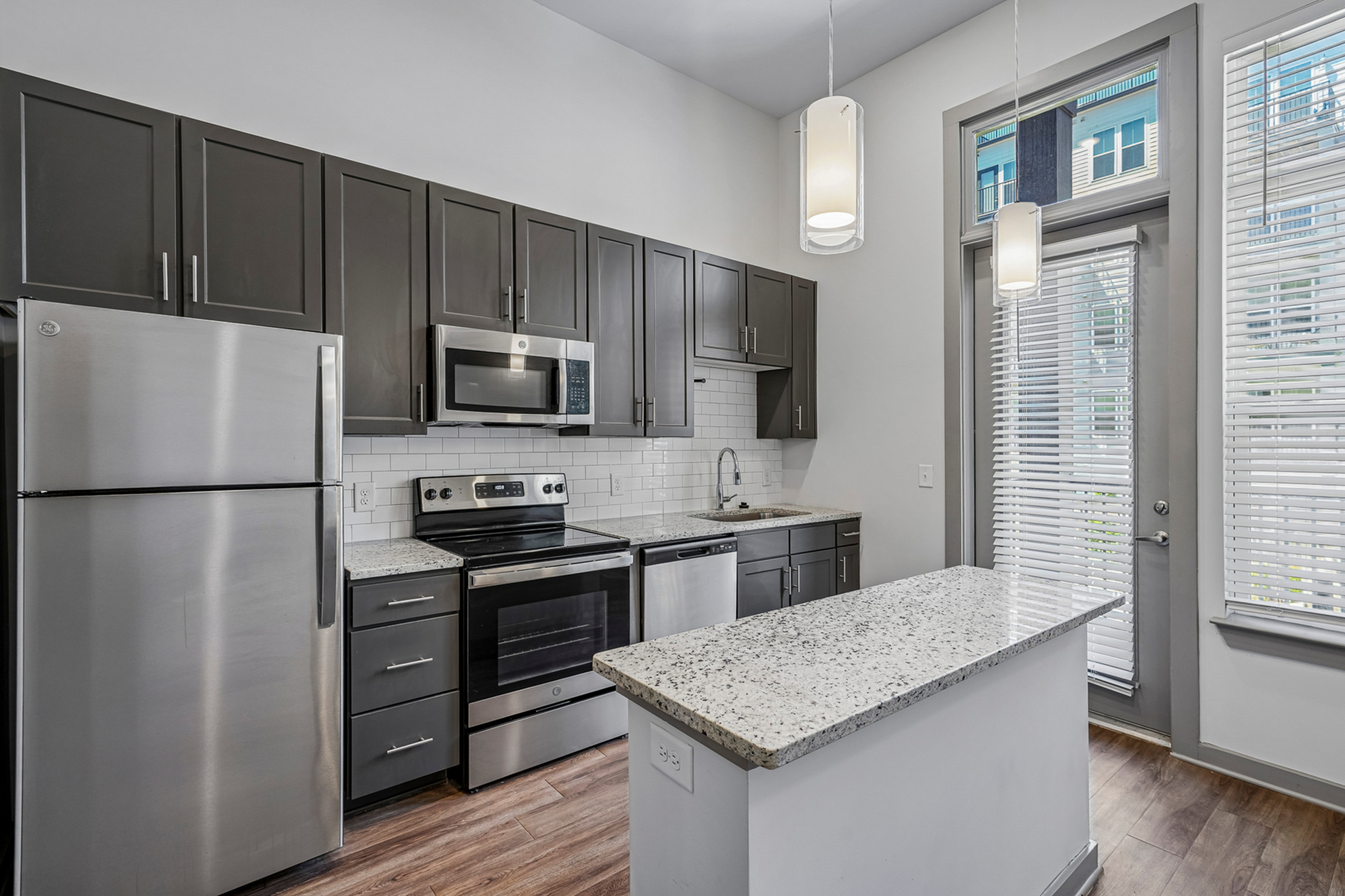 Modern kitchen with sleek dark cabinets, stainless steel appliances, and a stylish granite countertop island, illuminated by elegant pendant lighting.
