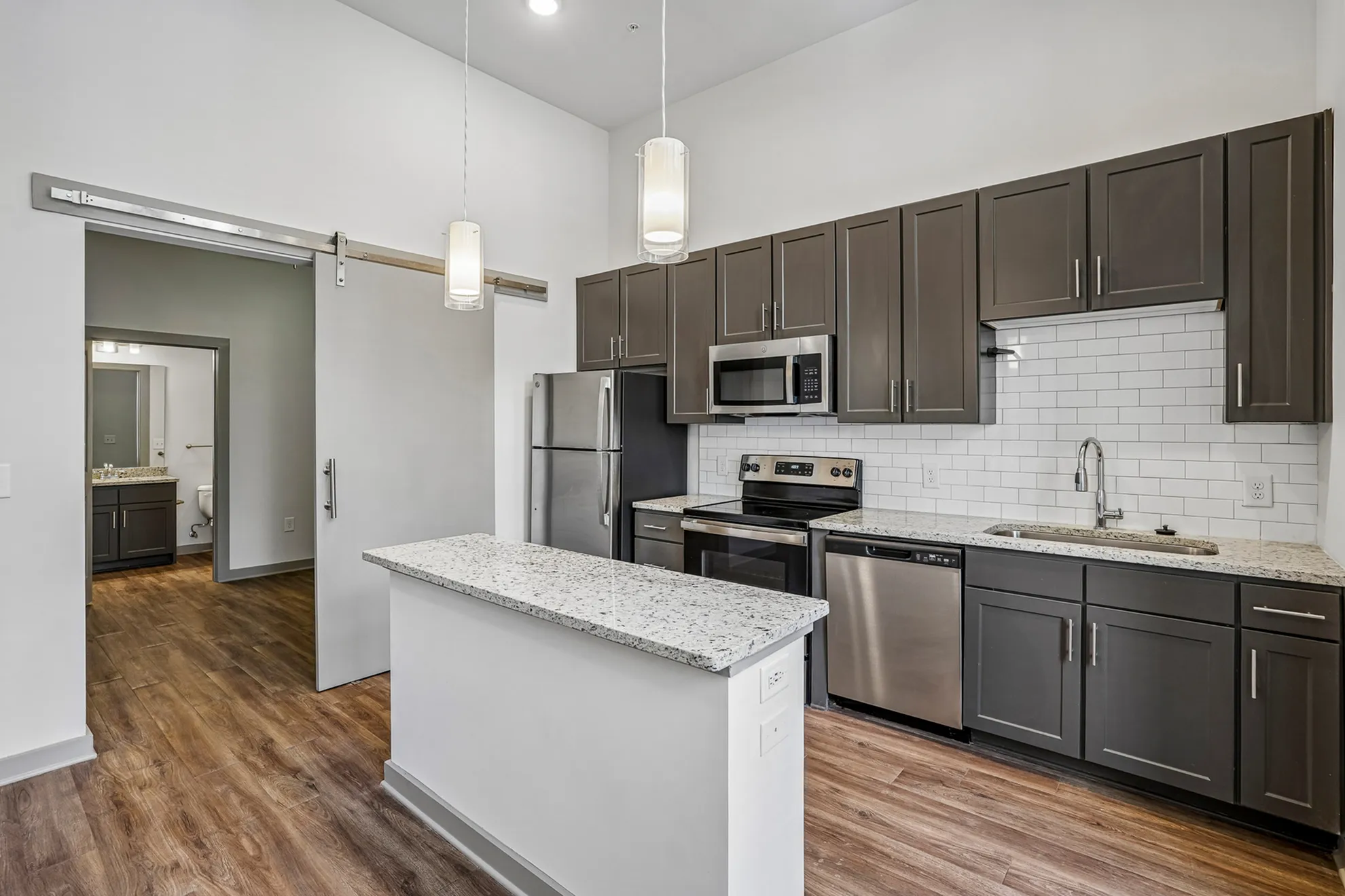 Modern kitchen with sleek gray cabinets, stainless steel appliances, and elegant pendant lighting over a granite-topped island, leading to a bright bathroom with sophisticated finishes.