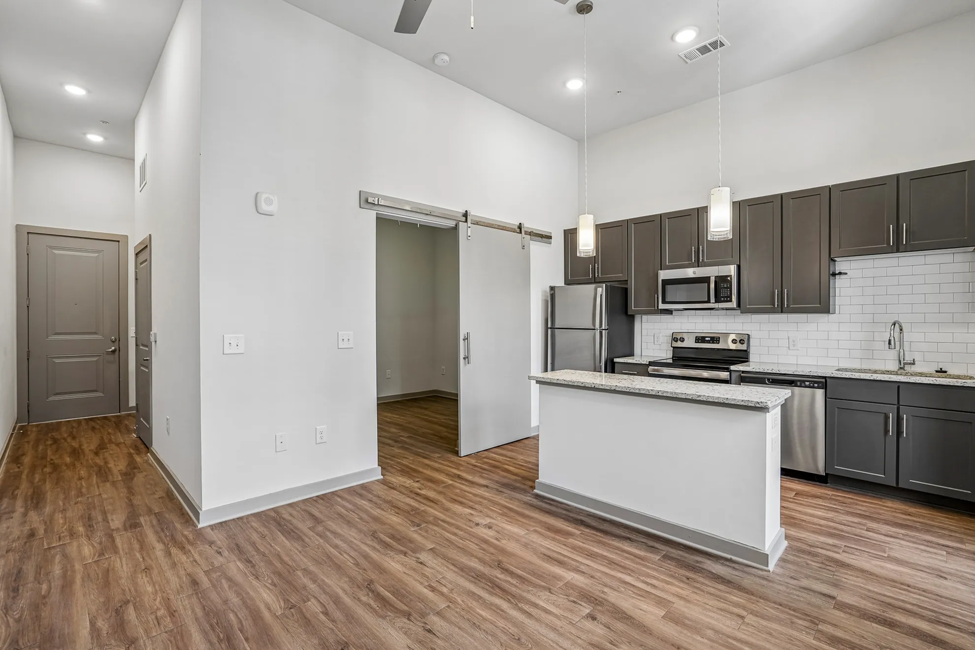 Modern apartment interior with sleek hardwood floors, a stylish open kitchen featuring granite countertops, stainless steel appliances, and chic pendant lighting.