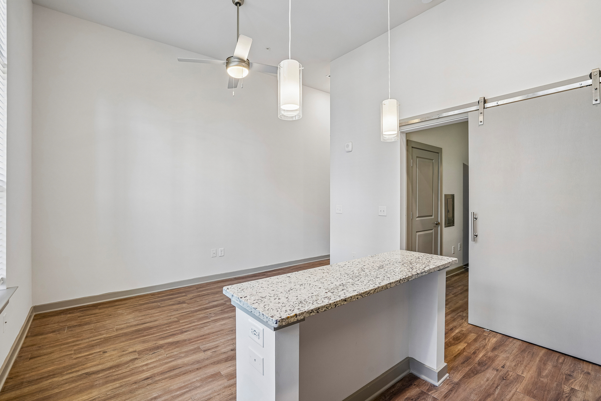 Modern apartment interior with sleek granite countertop and elegant light fixtures, featuring stylish wood flooring and a large sliding door for an open and airy feel.