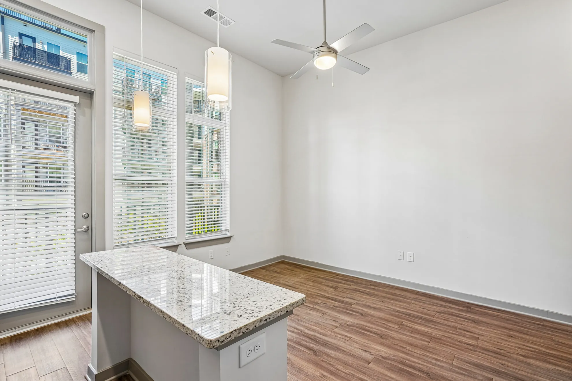 Bright and airy living area featuring large windows, elegant pendant lights, and sleek hardwood floors, complemented by a modern granite countertop.