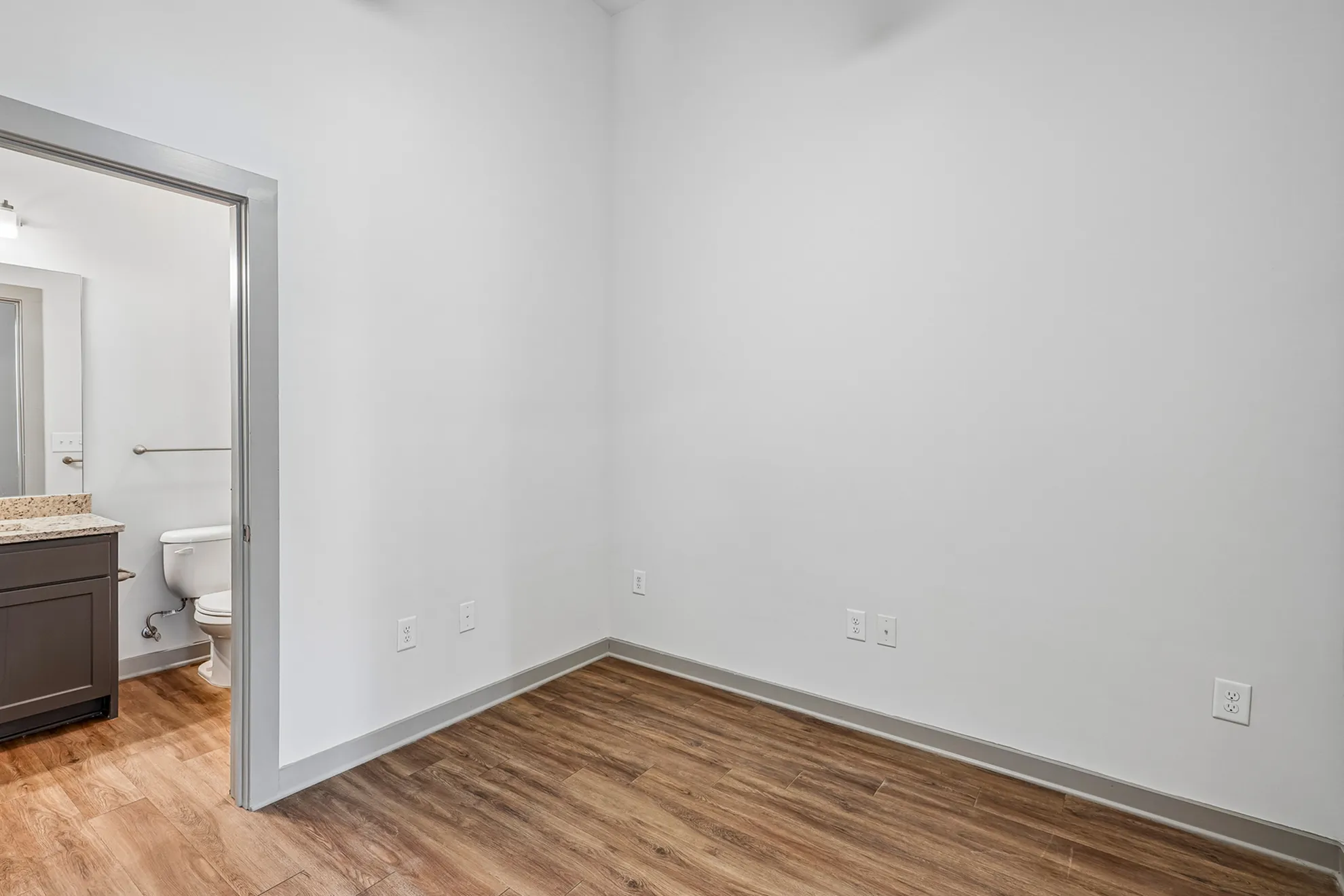 Sleek modern bedroom with hardwood floors and access to an en-suite bathroom featuring a granite countertop.