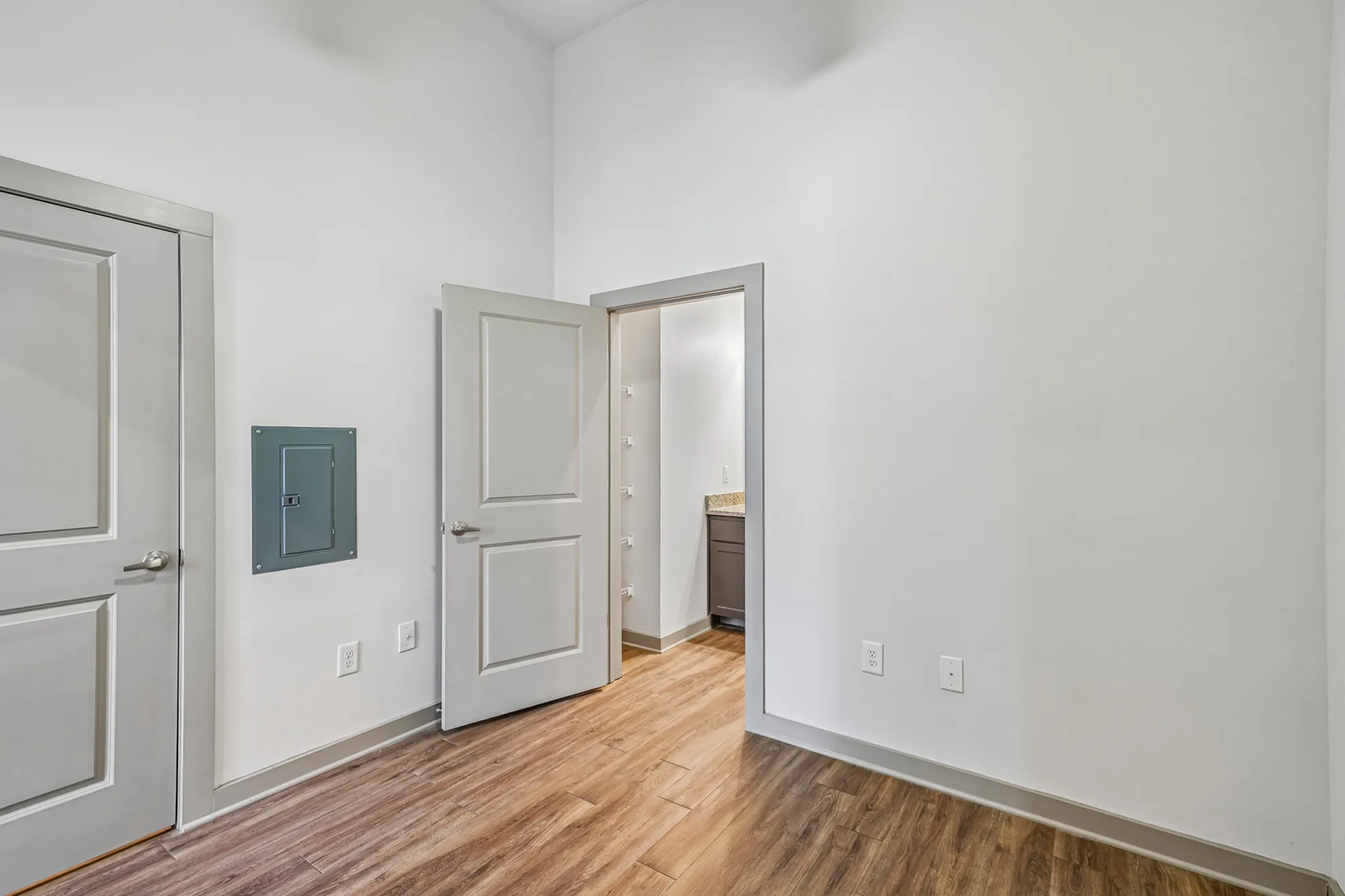 Modern apartment room with hardwood floors, white walls, and open door to a closet, offering a sleek and minimalistic design.