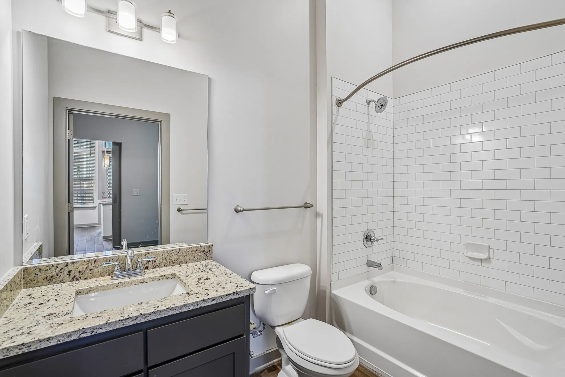 Modern bathroom featuring a sleek granite countertop, elegant vanity mirror, and a tiled bathtub with contemporary fixtures.