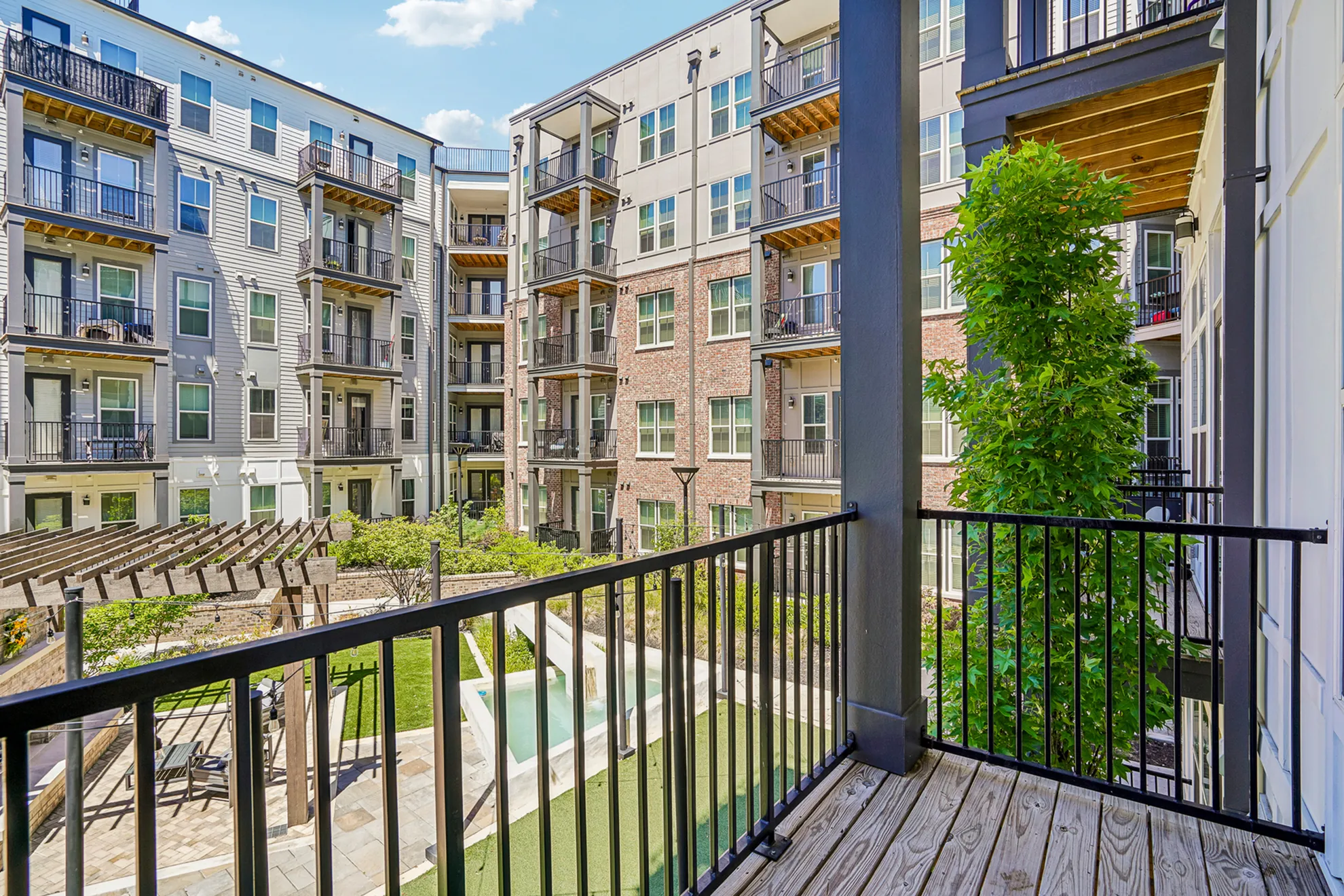 Charming apartment complex view from a private balcony showcasing lush green courtyard and modern architecture.