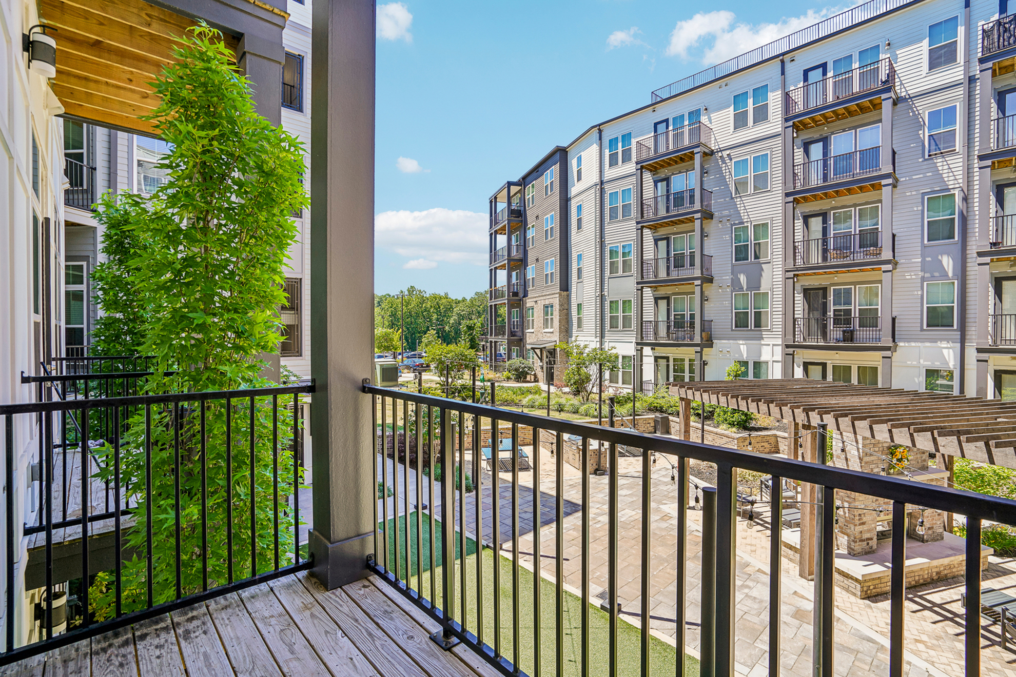 Charming balcony view of modern apartment complex with landscaped garden and sunny outdoor seating area.