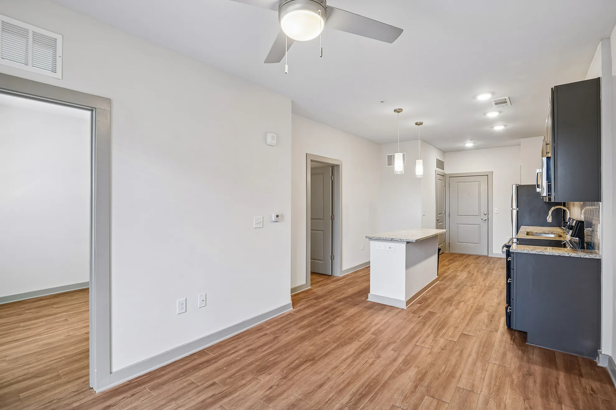 Modern open-plan kitchen and living area with sleek wood flooring, elegant ceiling fan, and stylish kitchen island perfect for entertaining.