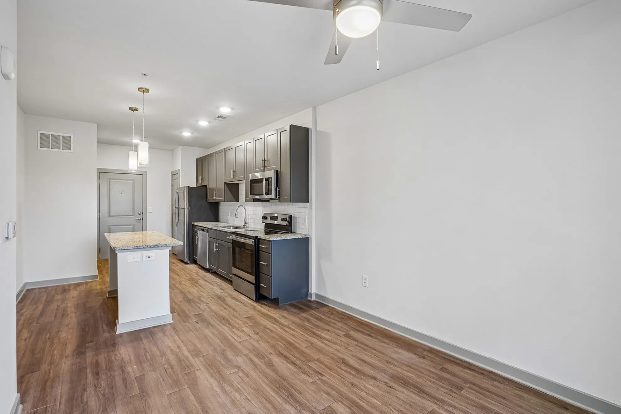 Modern open-concept kitchen with sleek grey cabinets, granite countertops, and stainless steel appliances, featuring chic pendant lighting and wood-style flooring.