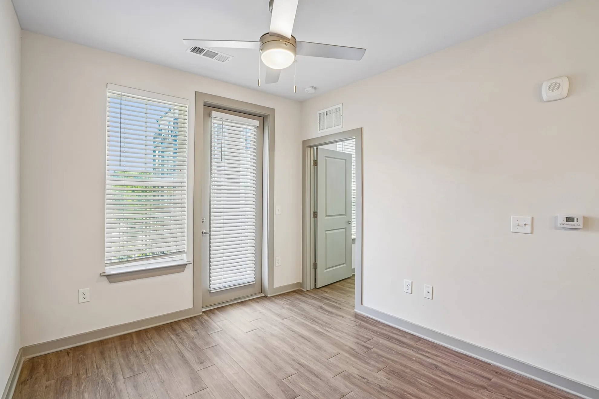 Bright and inviting room with large windows, a modern ceiling fan, and elegant wooden flooring.