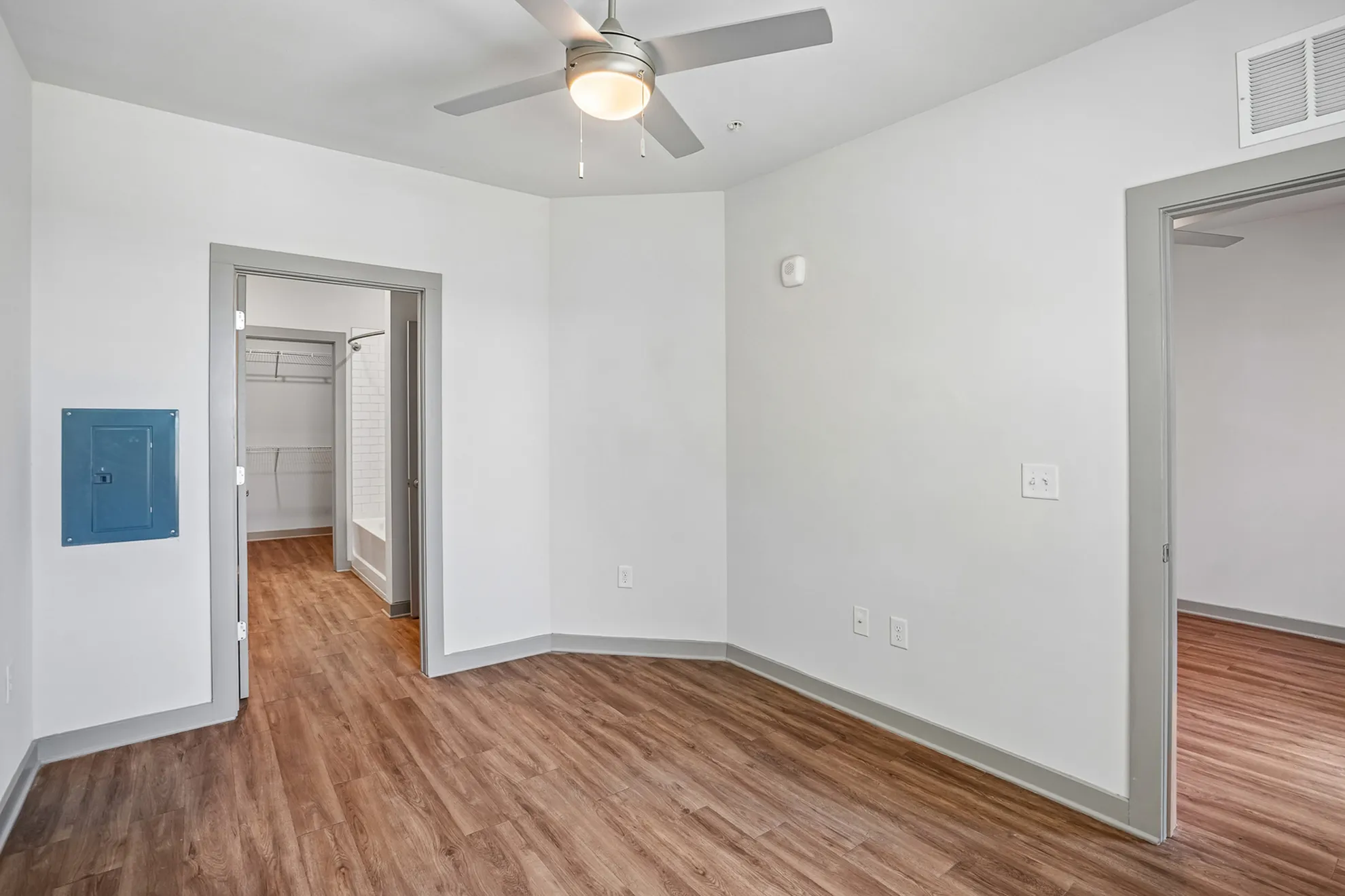 Bright and modern room with elegant wood flooring, featuring a ceiling fan and access to an en-suite bathroom and closet.