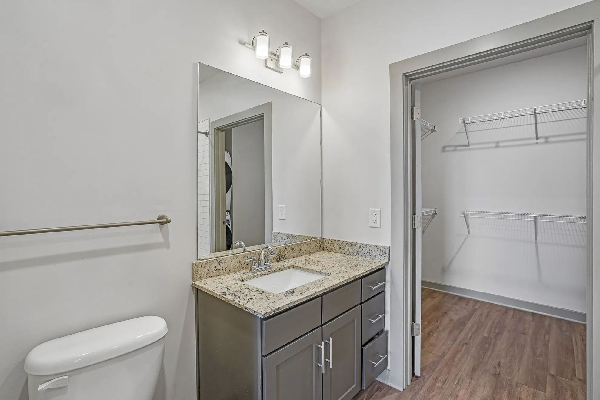 Modern bathroom with granite countertop, sleek storage, and adjacent walk-in closet.