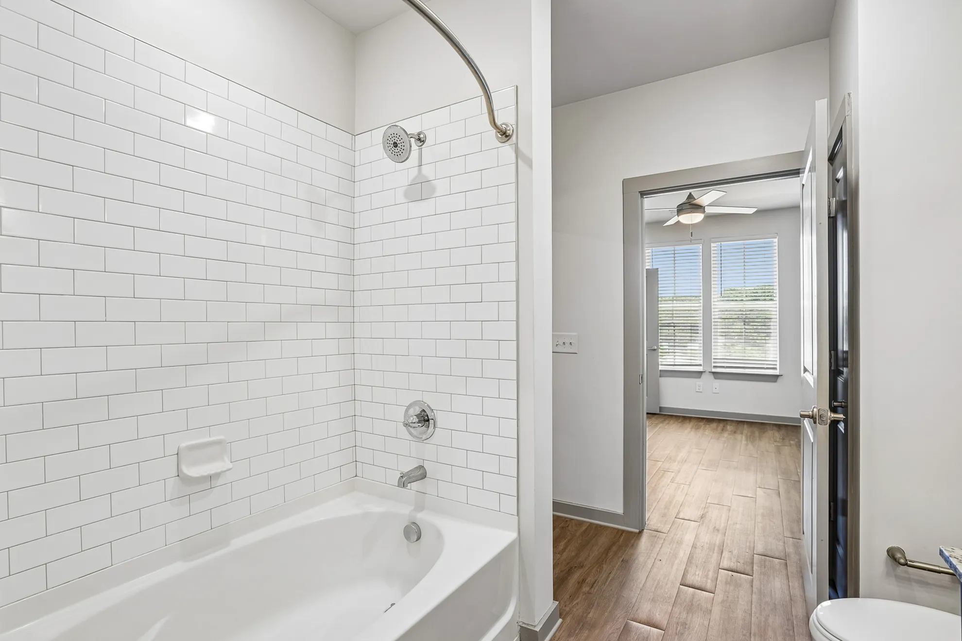 Modern bathroom with sleek white subway tiles and an inviting bathtub, leading to a bright bedroom with natural light and stylish wooden flooring.