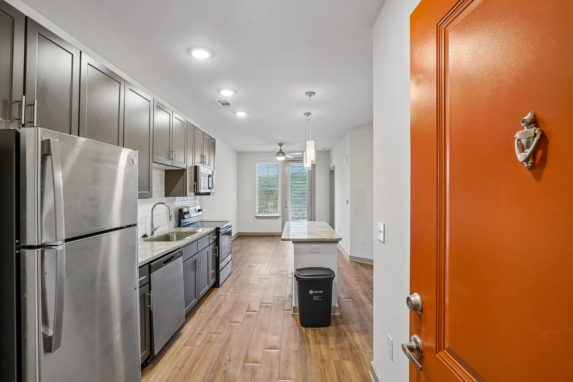 Modern apartment kitchen with sleek stainless steel appliances, elegant cabinetry, and a stylish orange door entrance.